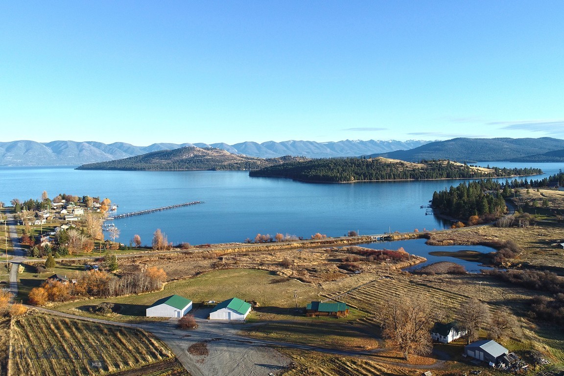 Experience one of the most versatile and visually striking properties on Flathead Lake. Set on 32.55 acres with 464 feet of premier waterfront, this estate combines privacy, scale, and functionality in a way that’s increasingly hard to find. Dayton Creek winds through the property, adding a rare natural feature that enhances both the setting and usability of the land.

The main lake residence offers 1,589 square feet with three bedrooms and two bathrooms, positioned to capture unobstructed views of Flathead Lake and Wild Horse Island. Designed for easy lake living, it features a custom rock fireplace, expansive deck, and seamless indoor outdoor flow for entertaining or quiet evenings looking over the water.

A secondary residence adds both flexibility and character. Originally built in 1908, the 916 square foot farmhouse includes one bedroom, two bonus rooms, one bathroom, and a 326 square foot finished attic. Surrounded by mature cottonwoods and a private yard, it offers a distinct setting for guests or extended stays.

The improvements on this property set it apart. A 3,132 square foot winery building includes a private saloon with lake views, a large shop and storage area with floor drains, two 1,200 gallon water storage tanks with irrigation to RV pad locations, and 200 amp electrical service. The 2,988 square foot venue building is designed for gatherings, featuring a glass overhead door, expansive windows with lake and mountain views, seating capacity for approximately 150 guests, ceiling sound panels, and an outdoor 25 by 60 foot patio with party lighting. Additional infrastructure includes a 30 by 40 shop and 33 gravel RV pads with water and electric.

Whether used as a private lakefront retreat, multi generational compound, event venue, or income producing investment, this property offers a rare combination of frontage, acreage, and built infrastructure on the LARGEST freshwater lake west of the Mississippi!