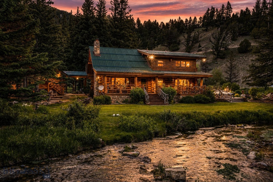 Water defines this property, with a spring-fed creek flowing year round, its current never silent, drawing elk, deer, birds, and trout to the banks and turning the grounds into a small working ecosystem. Just a short walk beyond, runs the Gallatin River and its blue-ribbon trout water, with the Gallatin National Forest bordering the property. 
 
This private river camp encompasses roughly 1.6 wooded acres across three parcels, and while all seasons are stunning, summer is the showstopper, when the water runs full and the grounds turn green. The landscaping is mature with stone paths, shaded sitting corners, and a series of landscaped water features whose pools and quiet falls were built to mirror the creek itself. Snow softens it in winter, spring runs the creek loud, and the evergreens hold their color through every month between. 
 
A custom log home anchors the property with 3 bedrooms and 3 baths, refined kitchen, and cozyliving room. A separate guest cabin holds 2 bedrooms and 1 bath alongside the living room with a fireplace and full kitchen, room for family and friends without crowding the main house. A hand-hewn cabin dating to the 1800s lives on as a private den or artist studio, a single sitting room with an oversized chair and a built-in library and desk. When the weather turns, the independent screened family room carries the evening, with a game table, space to lounge, and a cocktail bar, all open to the sound of moving water. The detached two-car garage feels like a carriage house and is immaculate and worthy of any vehicle, finished with an epoxy floor, an enviable tool wall, and bonus space above accessed via a private stairway.
 
Minutes away are the shops, galleries and restaurants of Meadow Village and Town Center, with Big Sky Resort just a few minutes up the road. Few properties sit this close to town while bordering both forest and water, providing easy access to the great outdoors and fishing directly out your back door. 
 
A century of stewardship shaped this ground. The collection of structures, the water, the trees, all of it carries the marks of careful hands. The next chapter of 48500 Gallatin Road is unwritten. It waits for whoever arrives ready to write their own Big Sky story.