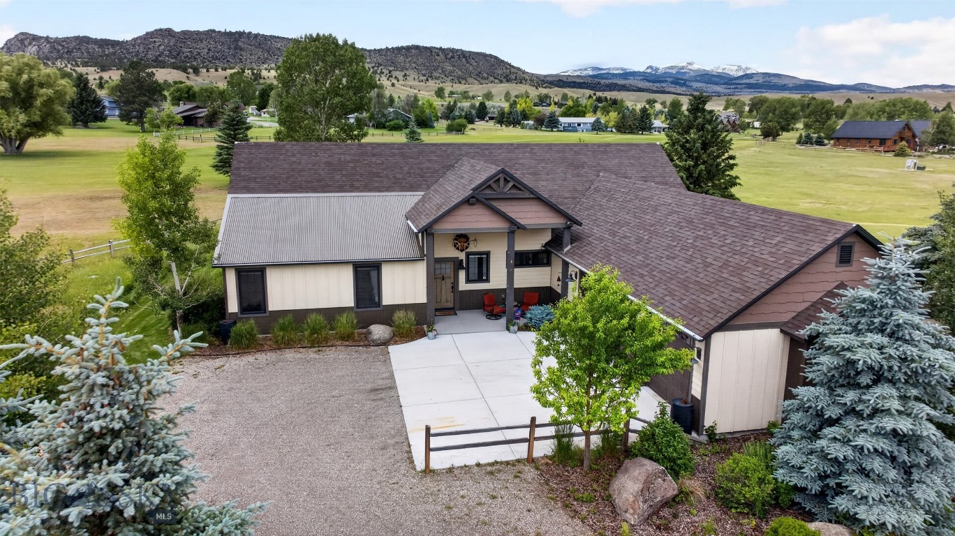 Exceptional custom mountain home showcasing timeless architecture, quality craftsmanship, and breathtaking views overlooking the 2nd fairway of Madison Meadows Golf Course and the Tobacco Root Mountains. The attractive exterior features Diamond Kote siding with board-and-batten accents, decorative timber beams, metal accents, a welcoming covered front porch, and a three-car courtyard garage with abundant storage. Designed for comfortable single-level living, the home offers a functional mudroom, separate laundry room, and an impressive great room with soaring 15-foot tongue-and-groove Knotty Alder cathedral ceilings, a gas Jøtul stove, and expansive mountain views. The beautifully appointed kitchen features Rustic Maple cabinetry, imported Quartzite countertops, a large center island, walk-in pantry, floating timber shelves, and premium KitchenAid stainless steel appliances with a gas range. The adjoining dining area includes a custom dry bar with wine cooler, creating an ideal space for entertaining. A 312-square-foot sunroom opens through a full-glass garage door to the covered patio, seamlessly blending indoor and outdoor living while capturing panoramic golf course and mountain views. Both spacious bedroom suites enjoy scenic views and Graber top-down/bottom-up cellular blinds. The primary suite offers dual vanities, a luxurious tiled shower, private water closet, and walk-in closet, while the guest suite features a private bath with a Kohler step-in whirlpool tub. Thoughtfully designed with exceptional finishes, outstanding outdoor living spaces, and an unbeatable location, this home offers the perfect balance of Montana luxury, comfort, and recreation.