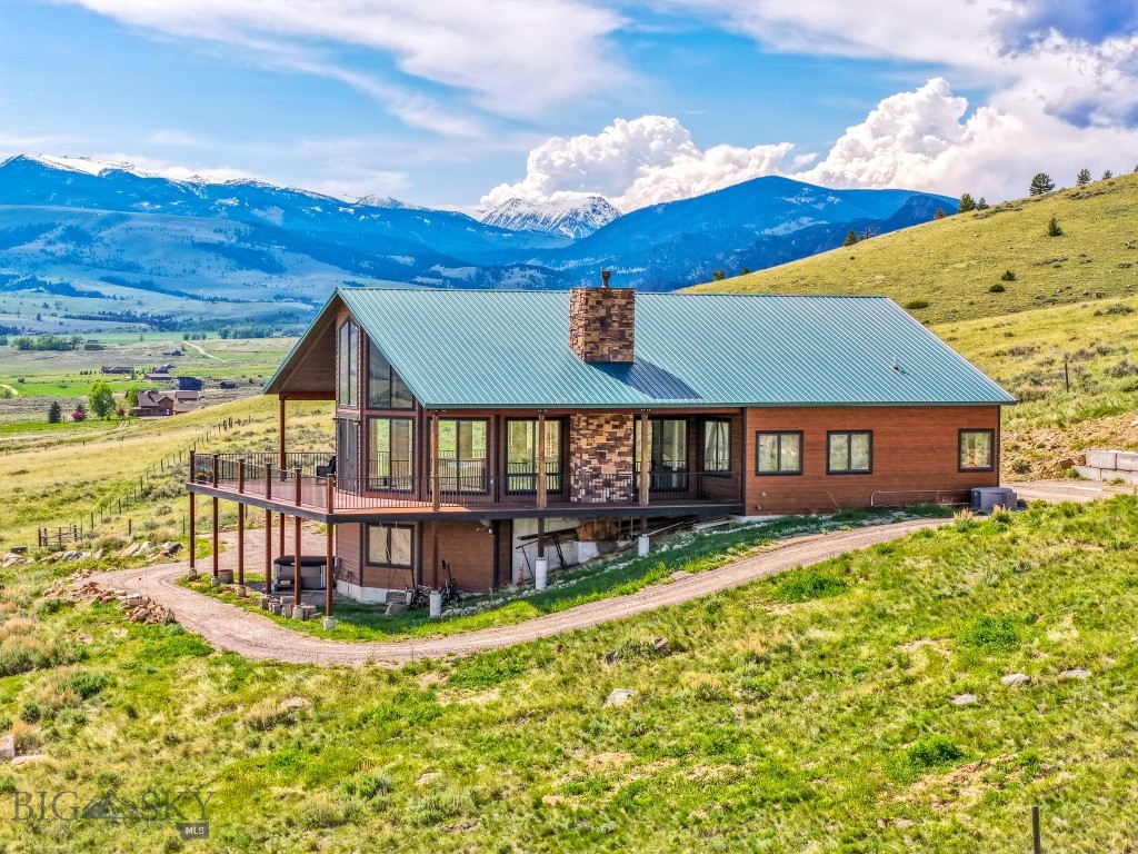 Where Mountain Views Meet Masterful Design: Situated on over 33 private acres above Ennis Lake, this architecturally distinct retreat offers panoramic views of the Madison, Tobacco Root, Gravelly, and Centennial mountain ranges—with visibility of the Grand Tetons on clear days. Now fully connected to power and utilities, the property delivers modern convenience without compromising its serene, off-grid feel. Designed to frame the landscape rather than compete with it, the home spans approximately 4,500 square feet. Vaulted ceilings and custom Big Timber trusses define the main living space, with hidden steel rods inside each beam to preserve uninterrupted sightlines in every direction. Hickory wood flooring and cabinetry bring natural warmth throughout, while radiant in-floor heating and a propane fireplace provide year-round comfort. The chef’s kitchen features granite countertops, premium appliances, and generous prep space—ideal for entertaining or everyday living. A custom Texas Mesquite mantle, milled from a 109-year-old tree, adds character to the Great Room. Expansive wraparound deck and patio extend the living space outdoors, and a brand-new hot tub offers a stunning perch for sunrise soaks or stargazing under Montana’s big sky. Additional amenities include a finished basement, an oversized attached one-car garage, and a detached two-car garage with extra storage. Zoning allows for up to three horses, making the property well-suited for equestrian use or quiet country living. Located just 20 minutes from Ennis, one hour from Bozeman-Yellowstone International Airport, and under two hours to Yellowstone National Park, this is a rare opportunity to own a legacy property that celebrates both craftsmanship and the raw beauty of Montana.