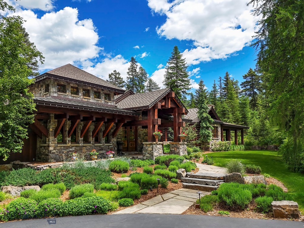 Located within the gated privacy of Whitefish Hills, 1263 Spencer Ridge takes full advantage of one of the best 20 acre lots in the development with views of the Whitefish & Swan Mountain Ranges and stunning views into Glacier National Park and Mt. Jackson. These views are celebrated from virtually every room in this timeless Montana residence of stone, timber and wood handcrafted around a thoughtful and efficient home design to a level of detail rarely experienced. This meticulously maintained home, shop & guest quarters, totaling 8405 SF of finished living space, is blended into the hillside and lives seamlessly with the outdoors from various decks and stone patios surrounded by mature landscaping, terraced gardens and a water feature whispering falling water to the private primary bedroom wing. A series of connected trails makes it easy to venture farther from the home to enjoy the acres of thinned and professionally maintained forest and the serene shore of a shared lily pond below the home. Upon entry from stone steps set under massive timber trusses the home welcomes you with a feeling of warmth and comfort exuded from colors, textures and materials blended in a style of refined Montana rustic. Plaster walls, stained alder trim and doors, sturdy bronze hardware, wood burning stone fireplaces and distressed hardwood floors set the tone while being complimented by top of the line plumbing and light fixtures, appliances, cabinetry and stone countertops. The additional comforts of radiant heat flooring, central air conditioning, audio and controlled lighting systems round out the amenities of a truly custom home experience. From the main entry foyer the home flows into a comfortable open concert of great room, dining area, kitchen and sit up bar all accessing outdoor decks. An incredibly private main floor primary bedroom wing is connected by an impressive glass and stone gallery while the open stairwell makes the transition to the lower level with three additional ensuite bedrooms, family and game room, bar, gym, office, theatre and wine room. Connecting easily from the kitchen, the stone floor mudroom makes the transition to the large three car garage and full guest apartment, while the detached shop located a few steps from the main home adds additional toy storage with more guest quarters above. Complimented by the amenities of Whitefish Hills and shared access to Blanchard Lake this home and location are priced at a true value.