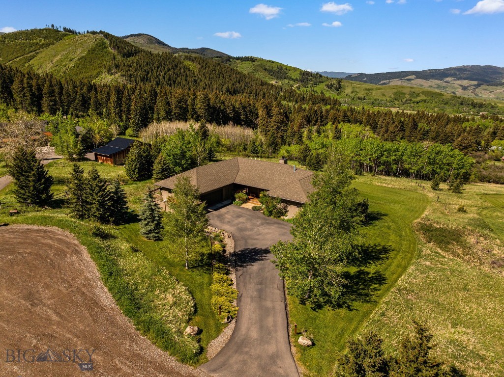 Tucked at the end of a quiet cul-de-sac on 2 private acres and perfectly positioned between Bozeman and Big Sky, this custom mountain home offers the rare combination of profound privacy and effortless access to world-class recreation. Surrounded by rolling hills, timbered ridgelines, and expansive mountain vistas, the residence was thoughtfully designed to frame the landscape as the focal point of daily life.

The main level is impressive and highly livable, featuring an open-concept that flows seamlessly from one space to the next. The heart of the home is the great room with a dramatic stacked-stone fireplace, exposed timber beams, warm wood floors, and walls of glass that capture breathtaking views from nearly every room. Natural finishes throughout create a comfortable, timeless feel.

The spacious kitchen offers custom wood cabinetry, granite countertops, a large island, stainless steel appliances, and a walk-in pantry. Just beyond the dining area, a separate sitting room provides a peaceful spot for morning coffee while overlooking the landscape. A dedicated den/office off the great room adds another beautifully positioned flex space with generous windows.

Privately situated on the main floor, the primary suite offers true main-floor living with direct outdoor access, two walk-in closets, and dual bath areas, including a luxurious soaking tub and a tiled walk-in shower.

The sun-filled walkout lower level adds two additional bedrooms, a spacious family room, full and powder baths, abundant storage, and a large unfinished area immediately ready for a future rec room, gym, or expanded guest quarters. With direct access to the covered patio and lawn, it works beautifully for guests while maintaining separation from the main living areas.

Outdoor living is a defining feature, with expansive decks, covered patios, and a level lawn extending the home into the landscape. Additional highlights include an oversized 2-car garage with workspace, ample parking, and gated area for campers, trailers, and all the toys that come with Montana living.

Rarely does such privacy coexist so gracefully with convenient access to Bozeman amenities, Big Sky skiing, and year-round outdoor adventures.