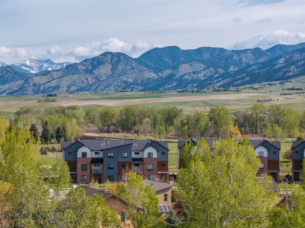 Framed by open green space with protected Bridger Mountain views, this modern 4-bedroom, end-unit townhome offers rare unobstructed Montana views and natural light just minutes from downtown Bozeman. Glen Lake Rotary Park sits directly across the street, offering a scenic lake for summer swimming and winter ice fishing, along with picnic tables and expansive open space.  The ground level features an oversized two-car garage, a flexible office suite or fourth bedroom, a full bath, and a welcoming entry. The second floor opens to a bright, contemporary living space where expansive glass sliders frame the mountains and create seamless indoor-outdoor flow. The kitchen is designed for both everyday function and entertaining, anchored by a waterfall quartz island, 36-inch gas range, walk-in pantry, and clean, modern finishes. Upstairs, a dedicated laundry room, additional en-suite bedroom, and a spacious primary suite provide separation and privacy. The primary retreat includes a gas fireplace and a well-appointed bath, creating a comfortable space to unwind.  Multiple balconies extend the living experience outdoors, capturing views of the surrounding open space and mountains. Located in Bridger Vale with REMU zoning, the property also allows flexibility for certain live/work opportunities.  With immediate access to trails, open space at your doorstep, and downtown Bozeman just minutes away, this residence offers a balanced blend of location, design, and long-term view protection.