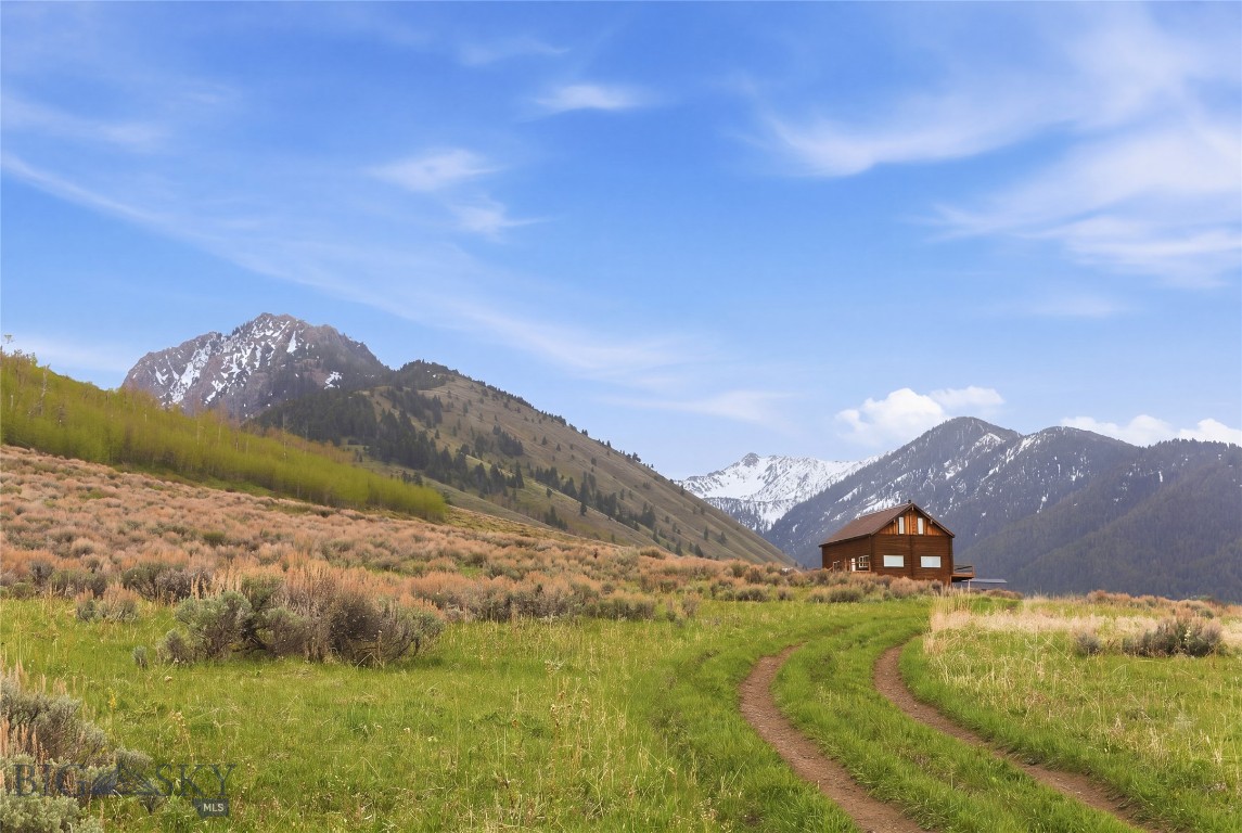 Perfect off-grid hunting and fishing retreat or family camp—set on 21 gorgeous acres bordering National Forest. This spacious 3,200 SF log cabin sits within walking distance of the Mile Creek Trail and offers expansive valley and mountain views through the large windows. Step out onto the wrap-around deck to take it all in.
A large, open-concept living room seamlessly joins the dining room and kitchen, anchored by a cozy wood stove that's perfect for warming up after a day outdoors. The main level primary suite features a private bathroom and opens directly to the deck. Upstairs, two additional bedrooms share a Jack and Jill bathroom. New flooring and fresh paint throughout give the cabin a clean, move-in-ready feel, and fiber optic internet runs right to the cabin—a rare bonus for a property this remote.
The daylight basement features a 1+ car garage plumbed for radiant in-floor heat, with plenty of extra space for toys, boats, storage, and hobbies. The lower level also houses the cistern and the Outback solar system with battery bank that powers the cabin, while a backup generator sits in its own enclosure outside. At 1,280 square feet, the lower level offers excellent potential to add finished living space down the road.
This Sportsman's Paradise sits in the heart of endless recreation and wildlife—with the Madison River, Henry's Lake, Hebgen Lake, Cliff and Wade Lakes, and Yellowstone National Park all within easy reach. Mostly seasonal access.
