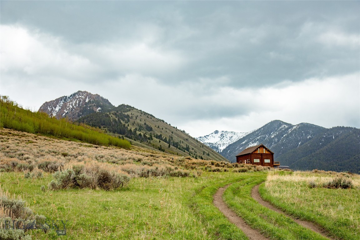 Perfect off-grid hunting and fishing retreat or family camp—set on 21 gorgeous acres bordering National Forest. This spacious 3,200 SF log cabin sits within walking distance of the Mile Creek Trail and offers expansive valley and mountain views through the large windows. Step out onto the wrap-around deck to take it all in.
A large, open-concept living room seamlessly joins the dining room and kitchen, anchored by a cozy wood stove that's perfect for warming up after a day outdoors. The main level primary suite features a private bathroom and opens directly to the deck. Upstairs, two additional bedrooms share a Jack and Jill bathroom. New flooring and fresh paint throughout give the cabin a clean, move-in-ready feel, and fiber optic internet runs right to the cabin—a rare bonus for a property this remote.
The daylight basement features a 1+ car garage plumbed for radiant in-floor heat, with plenty of extra space for toys, boats, storage, and hobbies. The lower level also houses the cistern and the Outback solar system with battery bank that powers the cabin, while a backup generator sits in its own enclosure outside. At 1,280 square feet, the lower level offers excellent potential to add finished living space down the road.
This Sportsman's Paradise sits in the heart of endless recreation and wildlife—with the Madison River, Henry's Lake, Hebgen Lake, Cliff and Wade Lakes, and Yellowstone National Park all within easy reach. Mostly seasonal access.