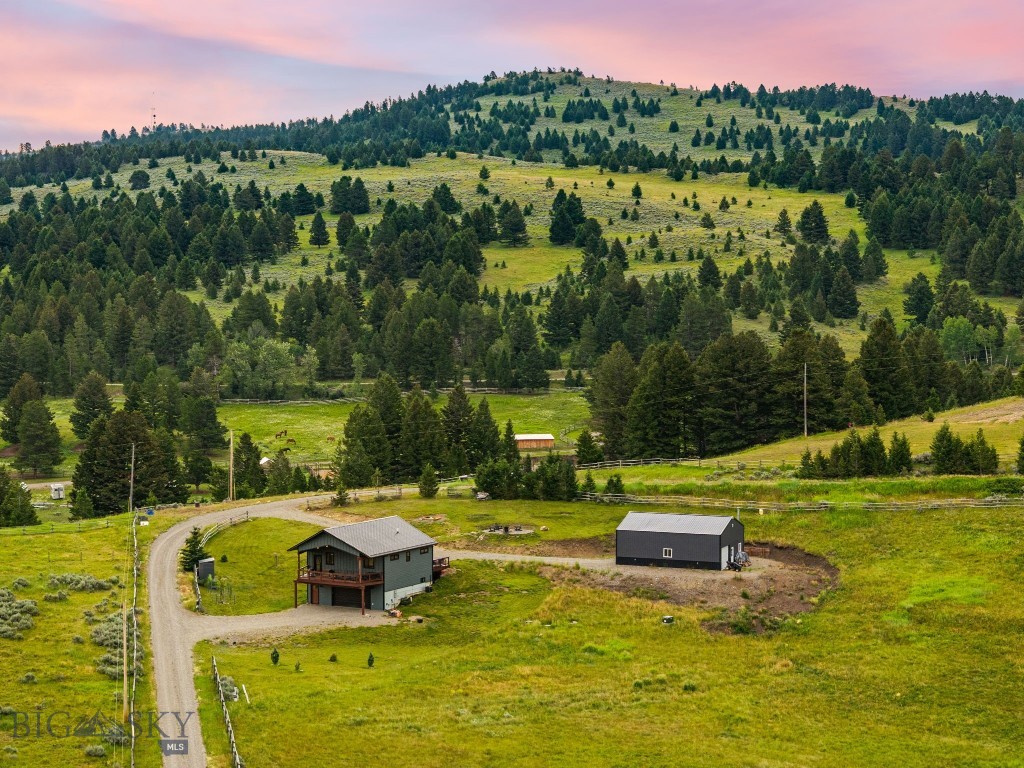Discover your private Montana retreat on 10.44 acres of breathtaking Gallatin Valley landscape. Built in 2022, this meticulously maintained 1,468 sqft. single-family home offers 2 bedrooms, 2 bathrooms, and a versatile bonus room, perfectly blending modern comfort with timeless mountain charm. Just off the Jackson Creek exit of I-90, the property delivers easy access to Bozeman while feeling worlds away. The thoughtfully designed home features a bright, open-concept layout with stunning finishes. The gourmet kitchen impresses with sleek gray cabinetry, crisp white countertops, a large island, and high-end stainless appliances—ideal for casual family meals or entertaining. Expansive windows frame sweeping views of rolling hills, meadows, and forested ridgelines that glow at sunset.
Outside, the property truly shines. A 1,200 sqft. wood stove-heated shop provides ample space for projects, vehicles, or storage. The land is an ideal horse property with two natural watering areas, lush pastures, and room for an additional home or guest house (subject to approvals). Timberline Creek, a year-round running stream, winds through the acreage, creating a tranquil water feature and abundant wildlife viewing opportunities.
Follow the pink-ribboned trail through the trees to a charming wooden bridge leading to the creekside fire pit area. Gather with family and friends around the crackling fire — perfect for stargazing, storytelling, and making memories under big sky sunsets. Located just 17 minutes drive from Bridger Bowl Ski Area, this slice of paradise offers four-season recreation: hiking, skiing, fishing, and more. Whether you