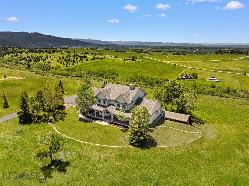 Perched atop a scenic bluff on nearly four acres adjacent to Bozeman’s coveted Triple Tree neighborhood, this exceptional property captures some of the most commanding views in the Gallatin Valley. Unobstructed 360-degree panoramas span the Bridger Mountains, Spanish Peaks, Tobacco Root Mountains, and the valley floor below, all with convenient access to downtown Bozeman. Thoughtfully positioned to embrace its extraordinary setting, the home offers covered front and rear porches that frame the surrounding landscape in every direction. From sunrise over the mountains to evening alpenglow, the views are exceptional in every season. Helping preserve the remarkable scenery, the property includes a ¼ interest in an adjoining 22-acre nature conservancy that protects surrounding open space and view corridors. Inside the home, a slate-tiled foyer opens to formal living spaces filled with natural light. Soaring vaulted ceilings and expansive windows define the main living area, where an oversized wood stove framed by custom built-ins creates a warm and inviting focal point. The space flows seamlessly into the kitchen and informal dining area, featuring custom maple cabinetry, tile flooring, and ample counter space, while the main-level primary suite offers comfort and convenience with direct outdoor access. Upstairs, three additional bedrooms enjoy expansive views, while a flexible bonus room adds versatility and additional living space, with access from both the main home and garage. Additional highlights include radiant in-floor heating, a water softener and filtration system, and a detached workshop ideal for hobbies or extra storage. With its extraordinary setting, this property presents an exceptional opportunity to personalize a home in one of Bozeman’s most desirable locations. Few properties combine acreage, protected open space, and panoramic views at this level.