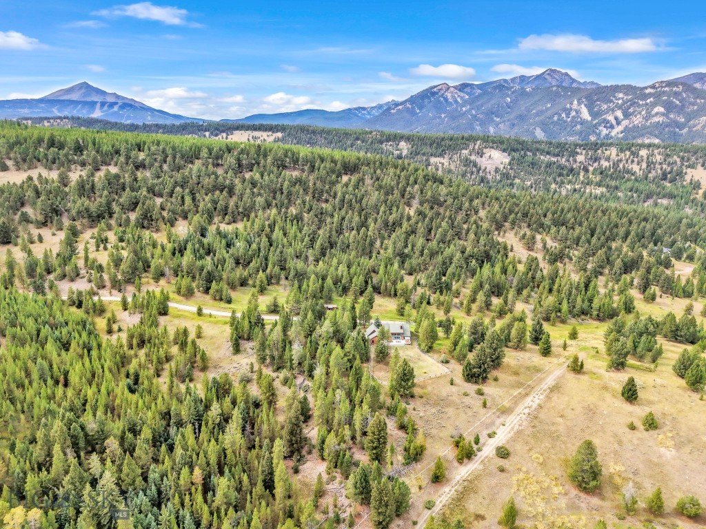 The private 20-acre getaway in Riverview Ranch offers serenity, seclusion, and breathtaking views. A full-length covered porch spans the front of the home, offering sweeping views of the south entrance to Big Sky. Step inside to a warm and inviting open-concept design, featuring expansive windows that allow natural light and breathtaking views of the Gallatin River and the Gallatin Mountain Range. The expansive deck, fenced yard, and a water feature create an idyllic setting for entertaining guests or enjoying quiet, peaceful moments. At the heart of the home, the great room features a floor-to-ceiling river rock wood-burning fireplace, along with vaulted wood ceilings. The functional kitchen is equipped with a gas Viking cooktop, double ovens, and ample dining space. Perfect for hosting dinner parties or casual get-togethers. Accommodations on the main floor, include a primary bedroom with an en-suite bath and walk-in closet, two additional bedrooms, a full bath and an office. A plus for hosting family and friends is the Bonus room with a private bath. Overlooking the Great Room, the spacious loft offers versatile space, currently used as sleeping quarters, an exercise area, and a game room. An attached two-car garage leads seamlessly into the mud/laundry room, providing a practical, functional transition from outdoor adventures to indoor living. Blending Montana Mountain living with modern comfort, this property delivers all, including elk, deer, birds, and other visible seasonal wildlife.