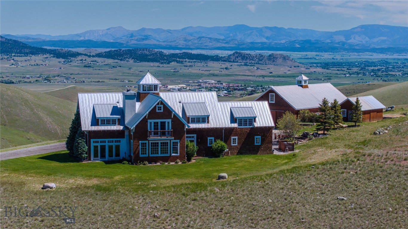 Set on 39.19+/- acres just 15 minutes from downtown Helena, this extraordinary Northwest coastal-inspired estate captures the rare balance of refined luxury, architectural character, and complete Montana privacy. Surrounded by sweeping 360-degree mountain views, the property evokes the timeless elegance of the Pacific Northwest, drawing inspiration from classic coastal lighthouses and the storied historic lodges of Washington’s Olympic Peninsula. A spacious foyer welcomes you into a beautifully designed 3-bed, 3.5-bath home featuring a dedicated office, gourmet kitchen with professional-grade gas range, granite countertops, and walk-in pantry. Open-concept dining and living areas are anchored by a striking wood-burning fireplace with raised hearth and rustic mantle. Large windows frame dramatic vistas throughout the home. An enclosed porch with flagstone floors and wood stove offers a cozy retreat for year-round entertaining. Refined rustic details include wide plank cherry flooring and exposed beams. The expansive primary suite boasts its own wood stove, private balcony, large walk-in dressing room, and a luxurious bath with oversized claw foot tub, double-head shower, Carrera marble counters, and separate vanity. A 2,880 sq. ft. fully equipped shop includes a kitchenette, full bath, 3-phase power (220/440), insulated roll-up doors, 7.5 HP air compressor, 1-ton monorail crane beam, and 220 welding power outlets throughout. Above, a 12