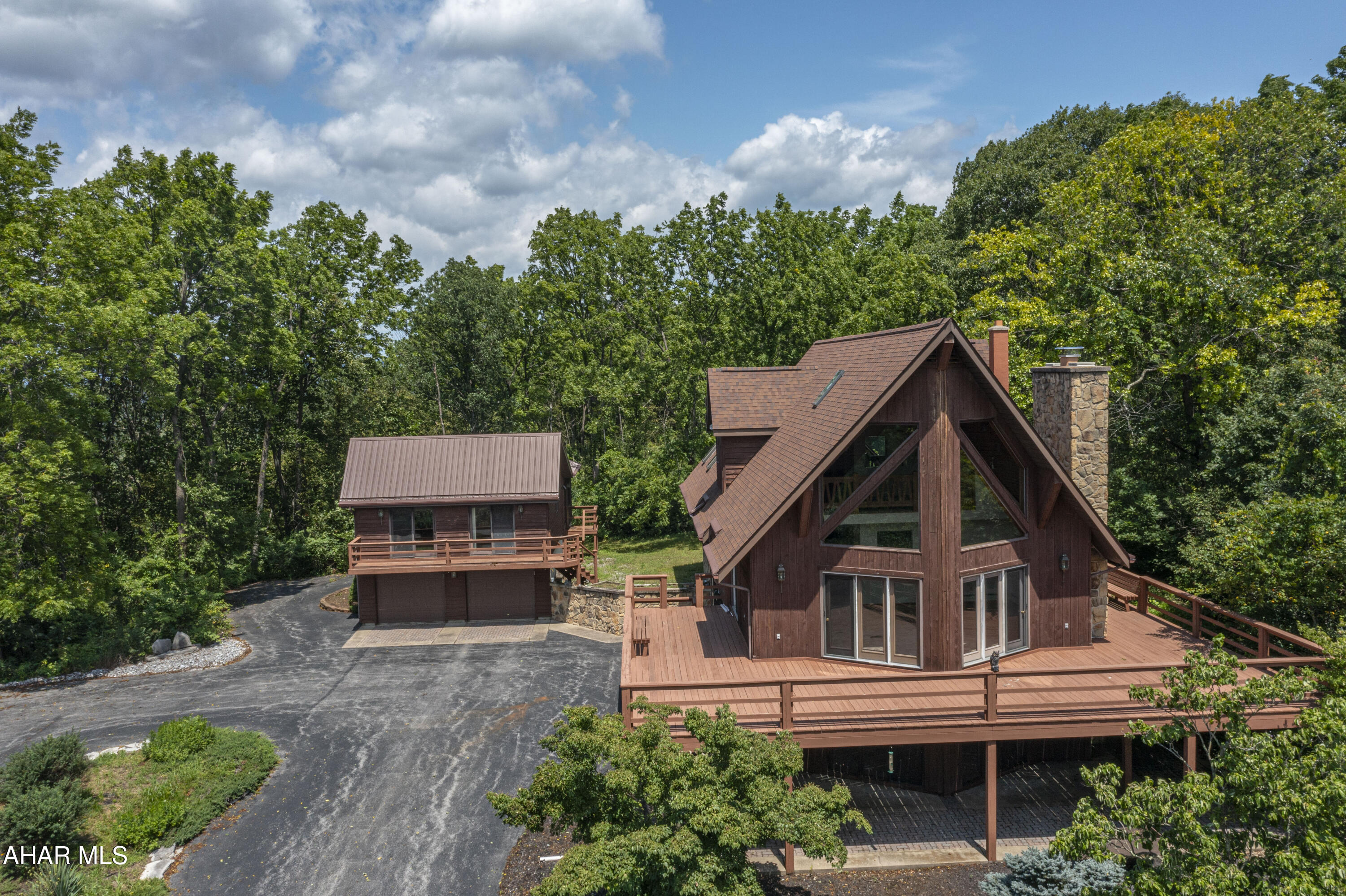 Welcoming and charming —this beautifully maintained, one-owner home sits on over 3 acres of peaceful land, offering unmatched privacy and stunning panoramic views. With a classic wrap-around deck and thoughtfully designed spaces both inside and out, this property is unique and a great opportunity to own a space with both comfort and versatility. 

Inside the main home, you'll find 3 spacious bedrooms and 3 full bathrooms, including a first-floor bedroom and bath. The living areas are surrounded by large windows that frame the scenic landscape, filling the home with natural light.

The finished basement offers cozy, extra living space centered around a gorgeous stone fireplace and includes its own full bathroom—perfect for entertaining or unwinding.

Additional features include:

Newer central air system for year-round comfort

Attached 1-car garage plus a circle driveway for easy access

Detached 3-car garage with a spacious apartment above—complete with a full kitchen, dining room, large living room, full bathroom, and 1 bedroom. A perfect setup for guests, rental income, or a private home office.