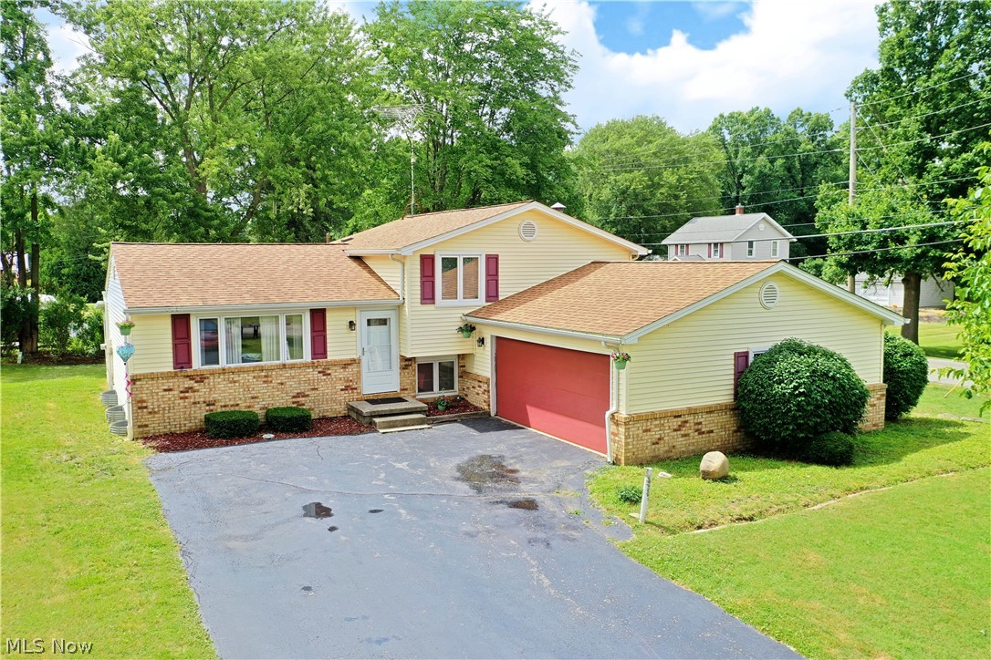 Enjoy the bright and inviting living space of this welcoming Mineral Ridge split level! The prominent corner lot perfectly highlights its attractive exterior complete with bold red garage door and partial brick façade. The sizeable yard wraps around to reveal the attached four-season sunroom. Inside, the recently updated interior delights with ash colored hardwood style flooring as the large picture window fills the living space with sunlight. A unique central fireplace divides the cozy dining area sat under bespoke lighting. The robust kitchen brings offset countertops and a mix of stainless appliances. Nearby, the sunroom falls away for easy summertime dining or relaxation. Upstairs, the three-bedroom design includes a lovely full bath  that offers private access to the master bedroom. Below, the sub level family room spans carpeted flooring as its stone mantle awaits near garage access with a second fireplace. Laundry, office space and a half bath complete the floor. The painted and