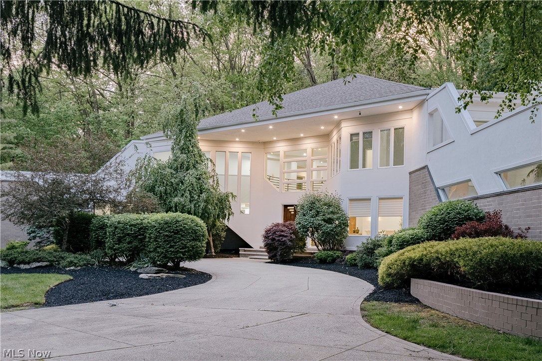 Tucked away on over 4 secluded acres just steps from the Chagrin River, this striking contemporary estate stands in a class entirely its own.  A bold architectural statement unlike anything Moreland Hills has ever seen. From its commanding exterior lines to its artfully conceived interiors, every element reflects a commitment to design that is as rare as it is refined. A custom double front door opens to a dramatic foyer where hardwood floors flow seamlessly into the formal dining room. The living and family rooms make an immediate impression: soaring two-story ceilings, expansive walls of glass that dissolve the boundary between interior and landscape, statement fireplaces, and rich wood accent walls converge to create spaces defined by light, scale, and architectural intention. The kitchen continues the design narrative with distinctive tile flooring, granite countertops, high-end cabinetry, and a tranquil eat-in nook framed by natural views. The primary suite is a private sanctuary unto itself.  A spacious retreat with a bonus room and balcony access, dual walk-in closets, and a spa-caliber bath appointed with exceptional finishes. Upstairs, a dramatic hallway connects three additional ensuite bedrooms and an open loft, each space thoughtfully integrated into the home's larger design story. The walk-out lower level is equally impressive, offering a fifth ensuite bedroom, billiards area, custom bar, media room, two bonus rooms, and sliding doors that open directly to the backyard patio, where indoor and outdoor living become one. This is not simply a home. It is a rare architectural experience, offering unparalleled privacy, refined luxury, and design-forward living in one of Moreland Hills' most coveted settings.