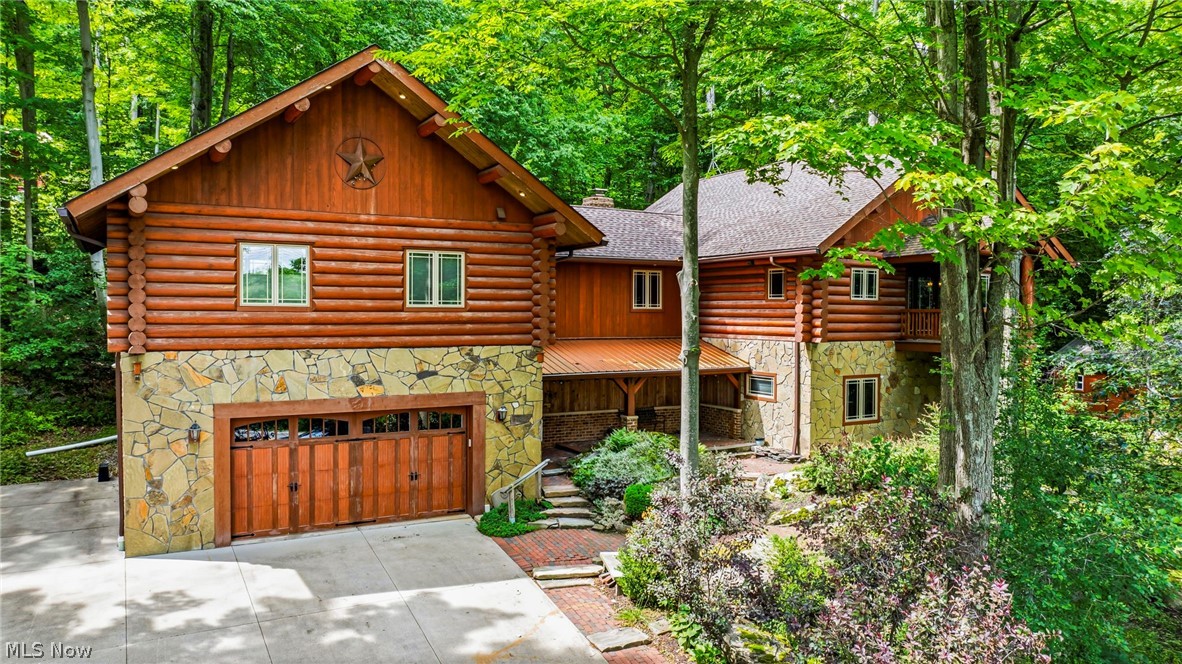 Welcome to a truly one-of-a-kind custom log home nestled in the natural beauty of Chesterland.Impressive 3-bedroom, 2-bath raised ranch offers approximately 3,228 total square feet and combines exceptional craftsmanship, quality construction, and a setting that feels more like a mountain retreat than Northeast Ohio. Built by Neville Log Homes of Montana using Engelmann Spruce and Lodgepole Pine from British Columbia, this home was thoughtfully designed and built into the property's natural bedrock. Inside, you'll find stunning woodwork throughout, including beautiful custom cherry cabinetry and trim crafted from cherry trees harvested directly from the property. Engineered maple flooring, exposed timbers, and two distinctive fireplaces add warmth and character throughout the home. The upper level features a Napoleon wood-burning stove with stone sourced from Utah, while the lower level showcases a Rumford fireplace with a distressed cedar mantel. Comfort is provided year-round with radiant heated floors, including the garage, a newer boiler, forced-air heating, and central air conditioning.
Pella windows frame picturesque views of the surrounding landscape, while the expansive deck with its Virginia Ledge Stone fireplace creates the perfect setting for relaxing or entertaining. The heated garage and additional outbuilding with a concrete floor provide excellent space for hobbies, storage, or projects.The property itself is extraordinary, offering approximately 200 feet of frontage and extending over 1,500 feet deep toward the rear. Surrounded by mature trees, abundant landscaping, massive natural rock formations, and a scenic ravine, the setting creates the feeling of living in a treehouse immersed in nature.They describe it as "built like a tank with love and care," appreciating the craftsmanship, quality materials, and thoughtful details of stone, timber, brick, and landscaping found throughout.