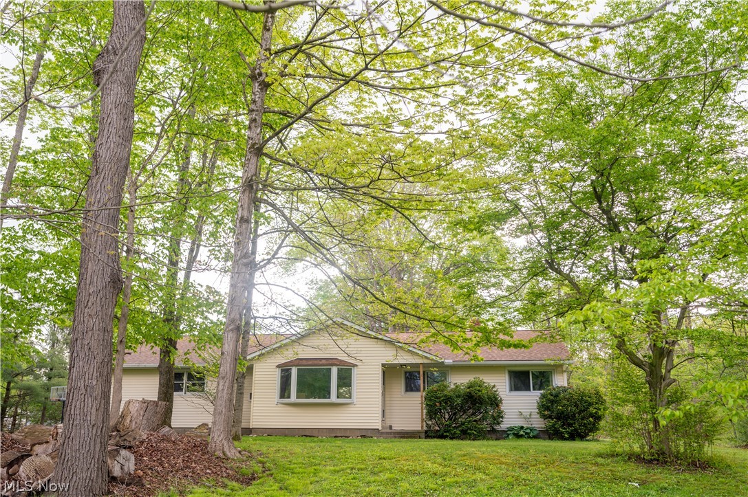 Nestled on 1.5 picturesque acres in sought-after Bainbridge Township within Kenston School District, this charming ranch offers the perfect blend of peaceful country living, thoughtful updates, and everyday convenience. Surrounded by mature trees and scenic views, this 3-bedroom, 1.5-bath home welcomes you with timeless character, warm hardwood flooring, and an inviting layout designed for comfortable living. Step inside to a sun-filled living room where a large front bay window fills the space with natural light. Hardwood flooring flows throughout the living room, dining area, and bedrooms. The beautifully updated kitchen (2022) offers modern finishes, abundant cabinetry, generous prep space, and a cozy dine-in area perfect for everyday living or entertaining. All three bedrooms are generously sized with peaceful backyard or wooded views. The full bath and convenient half bath offer everyday functionality. The full basement provides exceptional flexibility with abundant storage, laundry area, workshop space, and a separate family/recreation room highlighted by a stone fireplace—perfect for movie nights, hobbies, or additional entertaining space. Step outside and enjoy the beauty and privacy of your own 1.5-acre retreat. Relax on the patio, garden, host summer gatherings, or simply enjoy the peaceful tree-lined setting. Major improvements provide peace of mind, including updated kitchen (2022), roof replacements (2019 & 2023), new well compressor (2024), well expansion tank (2025), water softener (2025), and reverse osmosis system (2025). Additional highlights include an attached 2-car garage, mature landscaping, private septic, and an ideal location close to parks, shopping, dining, and commuter routes. A rare opportunity to own an updated ranch on acreage in one of Geauga County’s most desirable communities.
