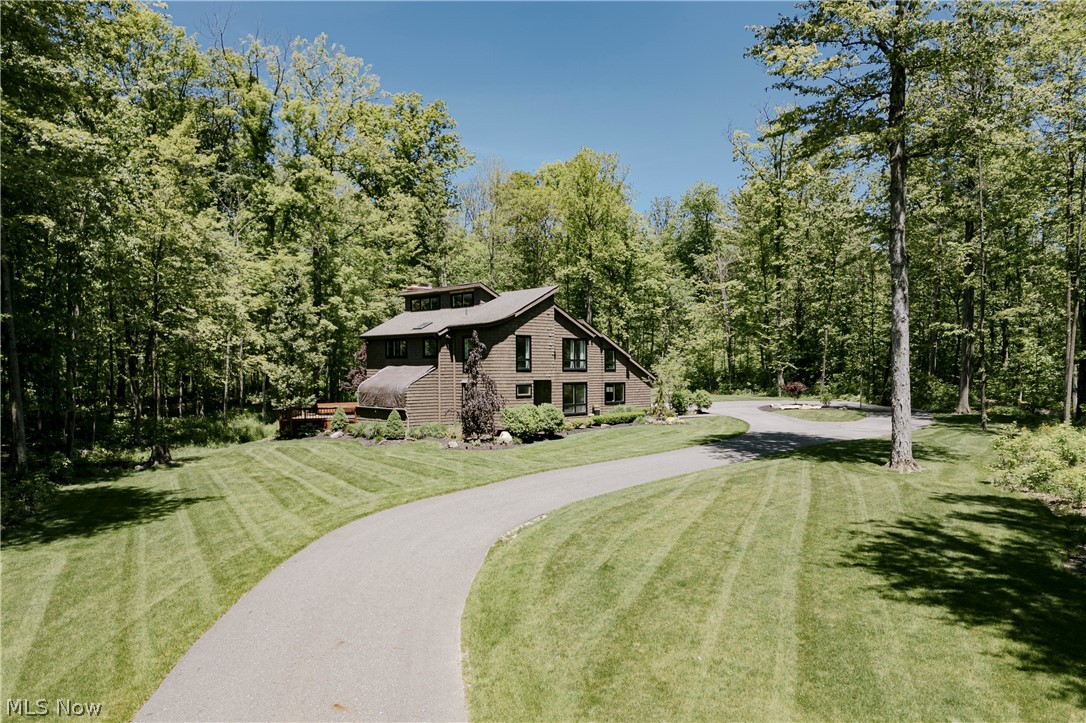 17138 Wood Acre Trl, Chagrin Falls offers beautifully updated modern living on a tranquil private lot surrounded by manicured gardens, lush lawn, and mature woods. A leaded glass front door opens to a dramatic two-story foyer filled with natural light and a grand staircase. Hardwood floors run throughout the main level. The kitchen features quartzite countertops, stainless steel appliances, updated cabinetry, tile backsplash, eat-in area, and pantry access. It opens to a formal dining room and a spacious living room with a stone fireplace, floor-to-ceiling windows, and sliding doors to a sun-filled solarium and expansive back deck. The main level also includes an updated laundry/mud room, a stylish half bath, and a spiral staircase leading to a separate upper-level wing. Upstairs, the second floor includes three bedrooms, including a spacious primary suite with fireplace, private loft, balcony access, walk-in closet, and fully renovated en-suite bath. A second full bath completes this level. A separate upper wing is accessible via spiral staircase or rear balcony but is not internally connected. It includes a loft overlooking the foyer, a bedroom, and a full bath. This space is ideal for guests, office, or multigenerational living. The partially finished lower level offers a rec room, two bonus rooms, an insulated wine cellar/storage room, and additional utility/storage space. Outdoor living includes an expansive backyard, large deck, hot tub, and shed. The setting is peaceful, private, and surrounded by nature.