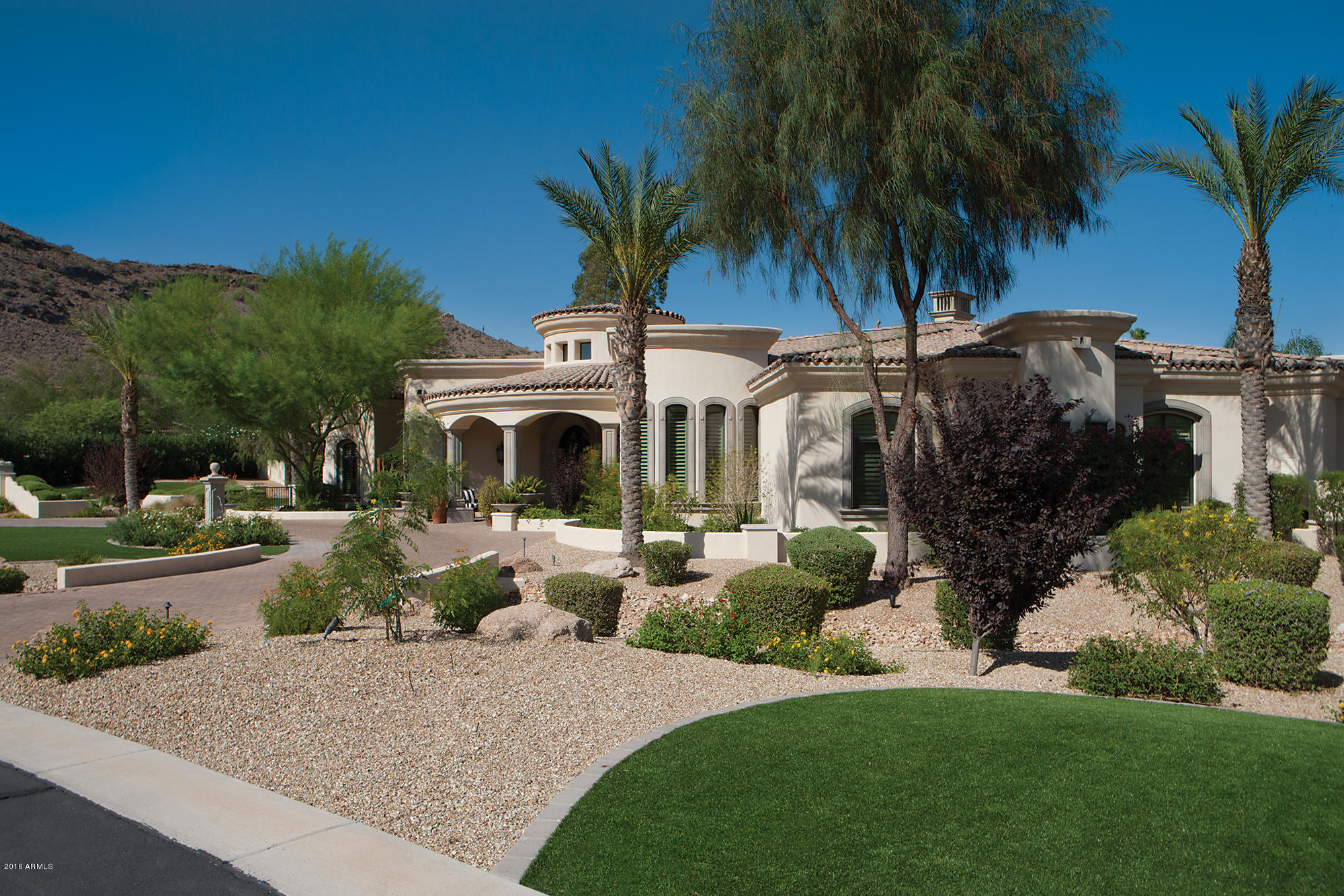 Exquisitely elegant, this sophisticated estate is snuggled in the shadows of Camelback Mountain. Custom-built beauty w/gated drive. Grand entry hall opens into sun-kissed living room w/volume view windows. Chef-quality kitchen w/magnificent movement-laden granite. Rounded wet bar that nuzzles up to sunlit family room. Library w/Camelback views. Secluded staircase swirls down to climate-controlled wine cellar. Opulent master retreat w/morning bar, dual couture closets, exercise/massage room, lavish bath w/steam shower. Plush state-of-the-art theater w/eight reclining chairs. Guest house w/private garage. Lush backyard w/stunning pool, dining/dancing patios, artificial grass, putting green, pretty trees/plants. Pool controls/exterior cameras controllable via smart-phone