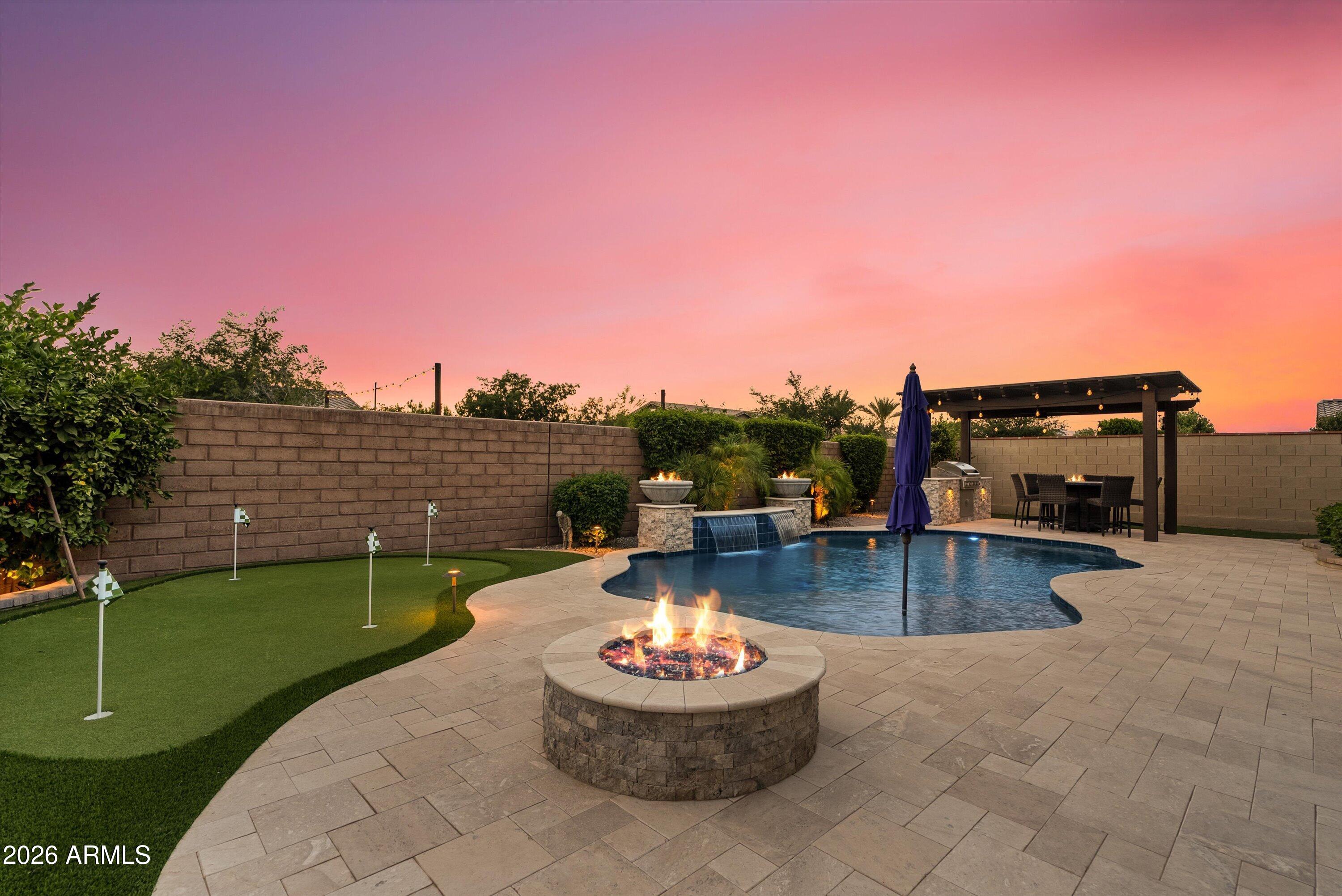 A rare offering in Eastmark's gated David Weekley community, this private corner lot home spans an expansive quarter acre with no rear neighbors, delivering unmatched space, privacy, and design. Elevated from the start, the interior showcases tall ceilings, abundant natural light, wood shutters, and a dramatic circular ceiling detail with chandelier focal point. The kitchen is built to impress with a large island, gas range, built-in oven, and custom tile accents that extend into the fireplace and office wall. Each bedroom features its own en suite bath, while the primary suite is designed as a true retreat with dual closets, a soaking tub, and oversized walk-in shower. The backyard is a standout, offering a fully finished resort-style setting with travertine pavers, heated and cooled pool with fire features, putting green, built-in grill with pergola seating, and remote patio shade. Opportunities like this are few and far between.