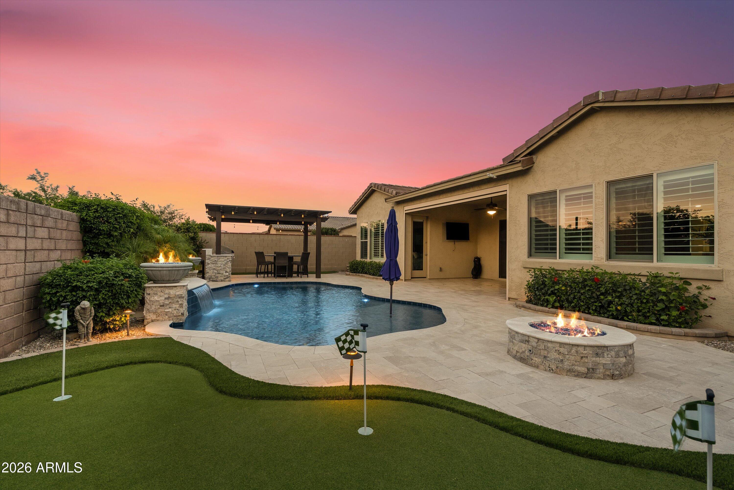 A rare offering in Eastmark's gated David Weekley community, this private corner lot home spans an expansive quarter acre with no rear neighbors, delivering unmatched space, privacy, and design. Elevated from the start, the interior showcases tall ceilings, abundant natural light, wood shutters, and a dramatic circular ceiling detail with chandelier focal point. The kitchen is built to impress with a large island, gas range, built-in oven, and custom tile accents that extend into the fireplace and office wall. Each bedroom features its own en suite bath, while the primary suite is designed as a true retreat with dual closets, a soaking tub, and oversized walk-in shower. The backyard is a standout, offering a fully finished resort-style setting with travertine pavers, heated and cooled pool with fire features, putting green, built-in grill with pergola seating, and remote patio shade. Opportunities like this are few and far between.