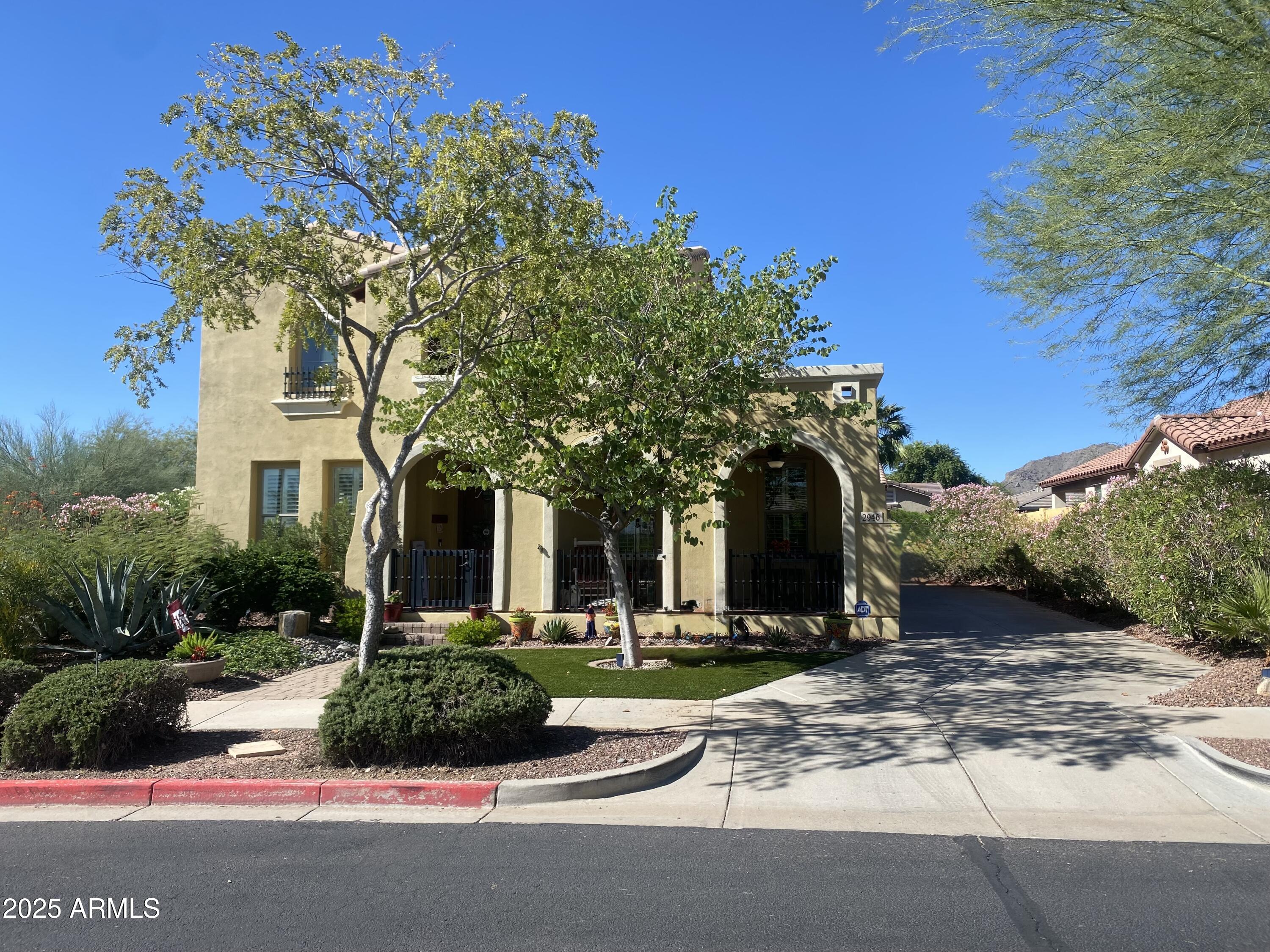 Welcome to your dream home in the highly sought-after Verrado community. This beautiful 5-bedroom, 4-bathroom home, adjacent to a green space & wash, offers the perfect blend of spacious living & unparalleled privacy, ideal for large families or those who love to host gatherings. This stunning property features lush front landscaping, a gorgeous orchid tree, & an inviting trickling water fountain. The expansive covered porch invites you into this beautiful home. AND in-place of the standard smaller den, this spacious home offers the rare OPTIONAL larger 5th bedroom downstairs with walk-in closet, with its' en-suite bath adding a 4th bathroom to the home, which together add several hundred additional square feet to the property. Welcome into the home's spacious entry, with the