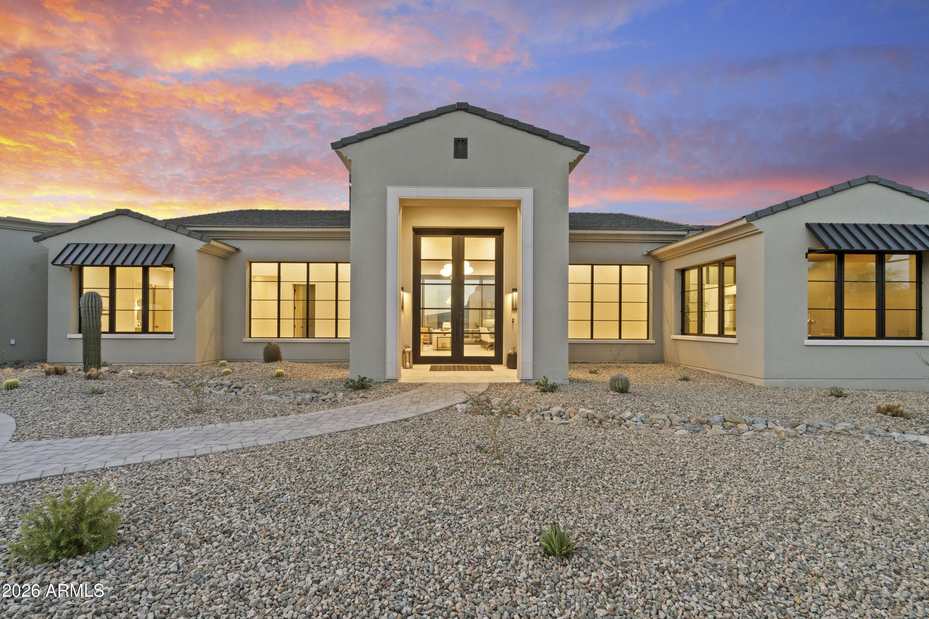 Pristine Custom Homes built an exquisite model that unfolds as a masterclass in architectural precision, intentionally positioned to capture the most commanding, unobstructed Superstition Mountain views available in Gold Canyon. Life here is defined by an effortless transition between the dramatic desert landscape and a world of ultra-refined interior luxury. Step through the monumental 12-foot entry door into a breathtaking great room scaled with soaring 14-foot ceilings, where a massive 12' x 20' expanse of Western glass frames the peaks like a living work of art. Every room is a sanctuary of light and scenery, complete with custom solid wood cabinetry, rich White Oak flooring, automated shades that seamlessly disappear into hidden ceiling trusses, and a dedicated TV pre-wire above the fireplace for effortless modern living. Additional thoughtful enhancements include rough-ins for motorized blinds in both the great room and media room, allowing for seamless future automation and ambiance control.

Designed for the culinary connoisseur and the consummate host, the chef's kitchen centers around a grand 12-foot Cambria quartz island, flawlessly integrated with Energy Star-rated Sub-Zero and Wolf appliances featuring convenient WiFi connectivity and smart-home control capabilities. A discreet custom pantry enhances functionality, while a convenient rough-in sink has been added to the island for future prep flexibility. The media room also offers a wet bar sink rough-in for elevated entertaining possibilities. As evening approaches, the home transforms into an ambient entertaining haven, illuminated by the glow of recessed mini-lights and under-cabinet LED accents, while integrated sound carries your favorite playlist from the indoor media room and dry bar out to the expansive terrace. A premium 4-stage reverse osmosis system further elevates the home's commitment to comfort, efficiency, and quality.

The outdoor lifestyle here is designed to celebrate the stillness of Gold Canyon and the majesty of the desert sky. Host unforgettable sunset dinners from the fully equipped 18-foot granite outdoor kitchen, complete with a premium built-in Yoder smoker, beverage fridge, dedicated sound system, and a natural gas rough-in at the built-in BBQ for effortless future customization. Afterward, unwind by the heated saltwater pool, listening to the elegant spillway of the elevated spa as the Superstition Mountains fade into twilight. Complete with a private outdoor shower, professional landscaping, and ample space for a future chipping and putting green, this is a sanctuary built for ultimate relaxation and effortless entertaining.

Even the automotive enthusiast is treated to unparalleled luxury, with a fully finished 2,004-square-foot space that feels like an extension of the home itself. This climate-controlled garage retreat features pristine epoxy floors, high-efficiency Mini-Split zoning, and its own integrated sound system. Designed with 12-foot ceilings and insulated 18' x 8' high-lift doors, adding custom car lifts to accommodate a world-class collection is an absolute breeze. For those with oversized adventure gear, the architectural design offers built-in flexibility: the architect has confirmed that the garage doors can easily be raised from 8 feet to 10 feet, creating a simple, straightforward modification to effortlessly accommodate tall vehicles, campers, or RVs. Tucked alongside the four-plus vehicle bays is a spacious, light-filled flex suite, offering an exceptional footprint for a private fitness studio, custom workshop, or high-end estate storage. Complete with a soft-water hose bib for flawless detailing, this space balances mechanical perfection with pure lifestyle utility.

Functionality meets luxury in the thoughtfully designed laundry room, which includes a secondary built-in desk ideal for a second office, study station, or creative craft room. Every detail throughout this remarkable residence has been intentionally curated to deliver a seamless blend of elevated design, smart-home convenience, energy-efficient living, and unforgettable desert luxury.