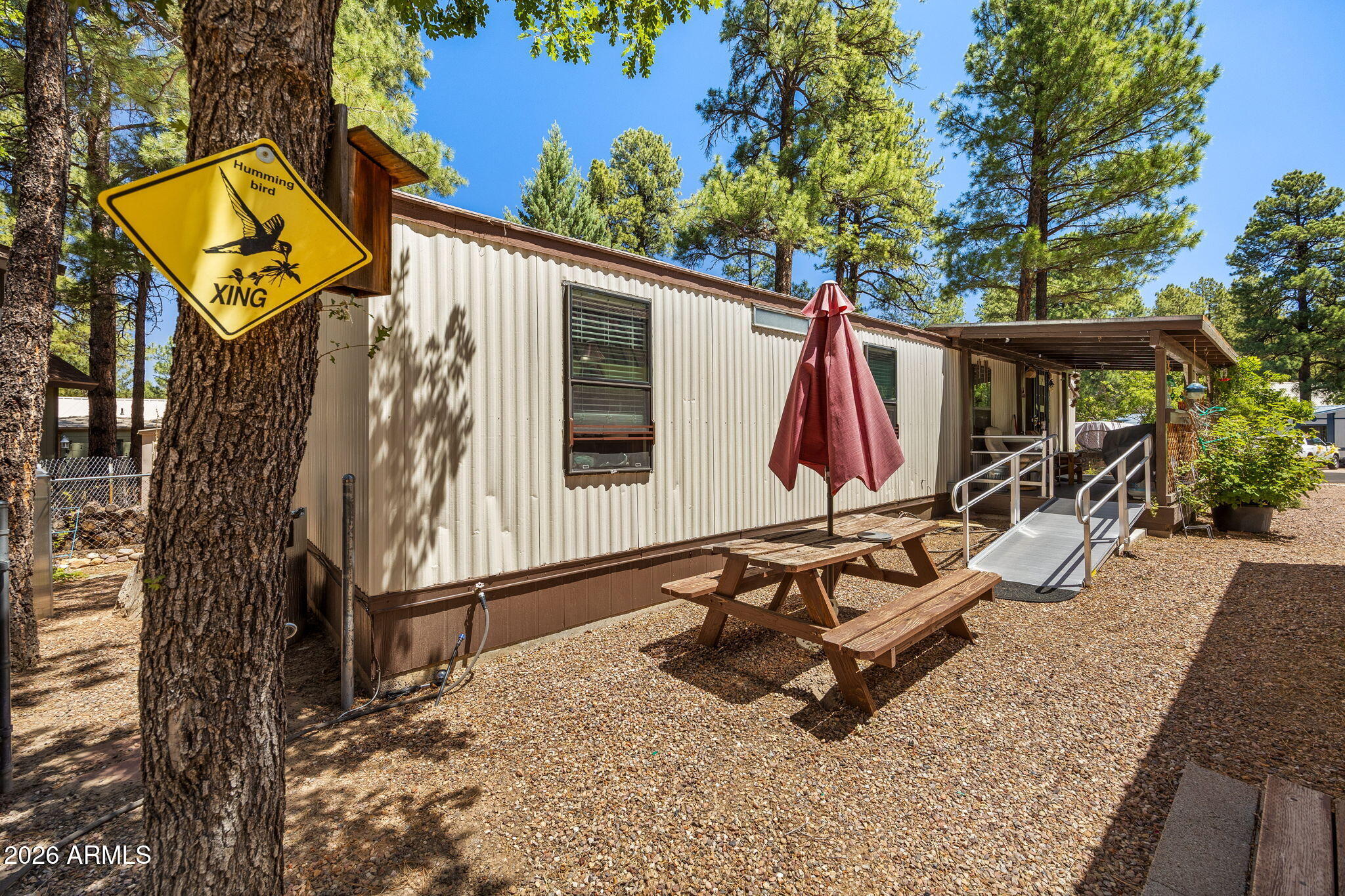 Set among mature ponderosa pines in Park Valley at roughly 6,300 feet, where the White Mountains give you real four-season weather. The covered front deck runs along the entry and is built for spending time outside, whether that's a quiet morning under the pines or an evening with friends, with step-free ramp access to the door.

Inside, the kitchen and living room open to each other in one connected space. The kitchen has hickory cabinets, a gas range, a stainless French-door refrigerator, a dishwasher, and a breakfast bar. Two bedrooms, one bathroom, and laundry in the hall.
The lot is fully fenced, chain-link in front and wood privacy fence in back. The tall-pine setting with open sun makes it a natural spot for growing things, with raised garden beds, a greenhouse, and mature trees already established, plus gravel parking with room for a boat or trailer. Outbuildings include a large storage building with a roll-up door and workshop bench, plus additional sheds.