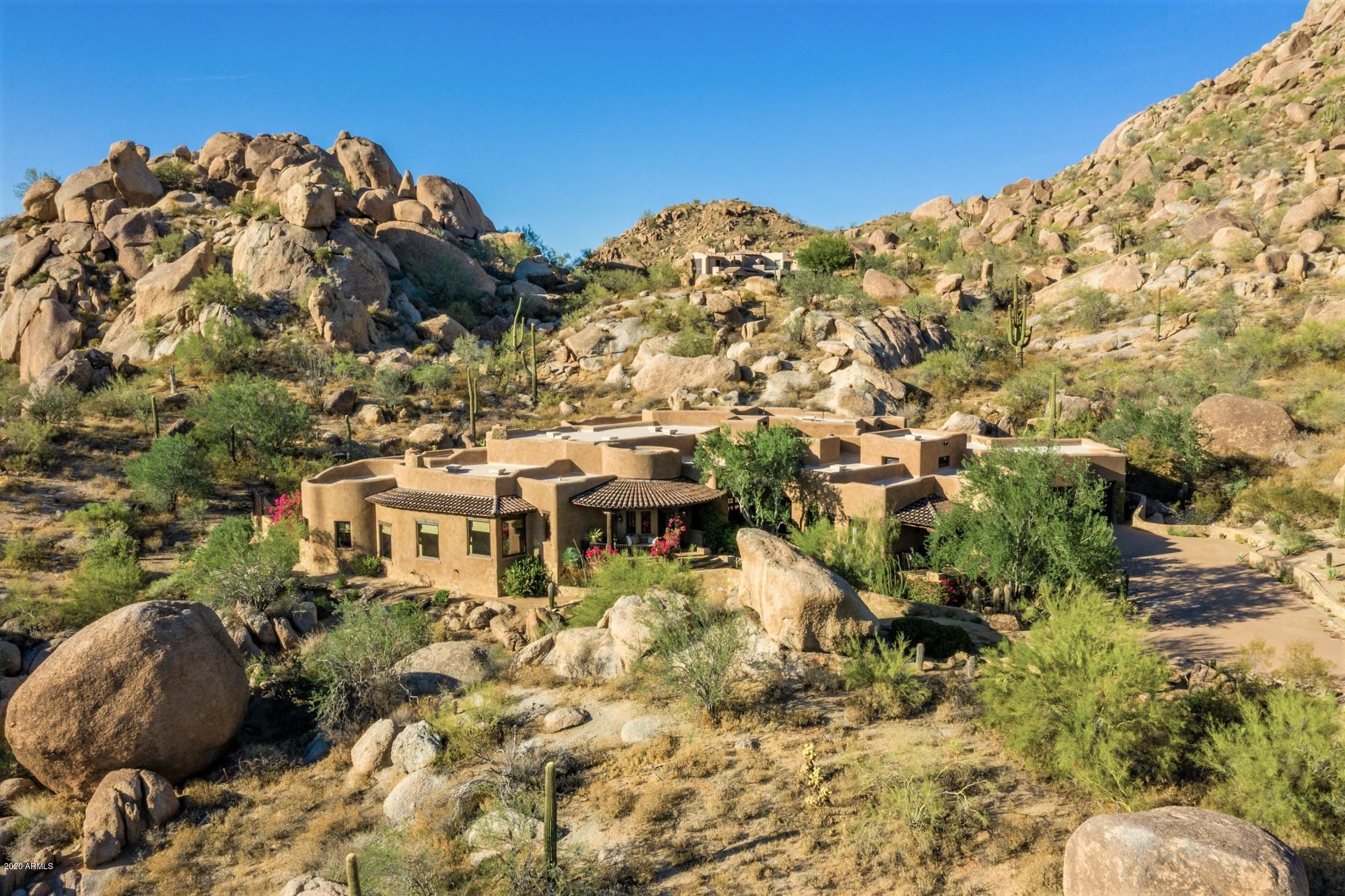 A Home like no other - A very special 6374 sq. ft.  custom built home by 3 of the Home & Garden ''Masters of the Southwest'' nested at the Southern rocky slope of Troon Mountain sitting on 3,7 acres, surrounded by massive boulders offering absolute privacy & spectacular desert views with city lights and breathtaking sunsets. A short walk over a manmade arched stone bridge leads to the inviting front porch. Entering the vaulted foyer is the beginning of discovering some of the many special finishes. Open great room with plank & beam ceiling. The open concept gourmet  kitchen is the heart of the house  with a master piece brick-walled cupola bringing beautiful day light, steel topped island, limestone counter top, hand painted tiles with pewter pieces backsplash and hood trimming. Materials have been used in the most unexpected way throughout the house. Floors are a mosaic of upside down variety size of Heritage Saltillo tile. The master suite is a true private sanctuary, very peaceful colors with its fireplace, private patio and antic stone trough fountain attached to the adjacent walled garden, spa like full bath with beautiful limestone floors, very unique curved shower with a window to the desert, his & hers closets. In addition, two comfortable guest suites, exercise room, Media room with fireplace and its own covered patio, writing room/office with fireplace and beautiful built-in stone desk, wine room, 2 powder rooms, laundry room and a bonus room for extra storage/den. Each has underground air recirculation. The backyard is an enchantment garden with a natural shape pool and streams of water running through the rocks, a built-in BBQ, and several shaded areas to sit, relax & enjoy the views in full privacy. *Check Video tour on photo tab.