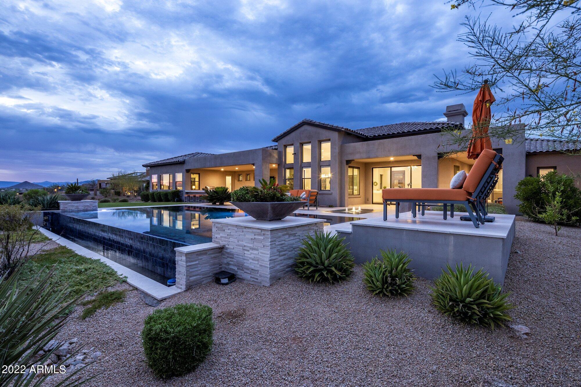 A sublime fusion of contemporary style with resort ambiance, this sleek sophisticated Talon Ranch home is a stunning setting in which to enjoy the finer things life offers.  Designed for the modern taste, a private courtyard with multiple covered patios welcomes you into this spacious retreat with a blend of hardscaping and thoughtfully placed vegetation, all centered around a firepit for cool desert evenings.  The custom glass front door opens to an equally inviting interior finished to a first-class level with custom chandeliers and recessed lighting accentuating vaulted ceilings, overlooking tile wood plank floors, electric fireplace with marble surround, gourmet kitchen with dual islands, dual ovens, Wolf range, all ensuite bedrooms and more.  The luxurious experience carries through oversized doors capturing panoramic views and opening to a tranquil outdoor living area with negative edge pool with spa, multiple seating areas for al fresco dining or entertaining, an outdoor kitchen, fire pit and simply a serene escape.  This spectacular gated community property brings the five-star resort experience home.