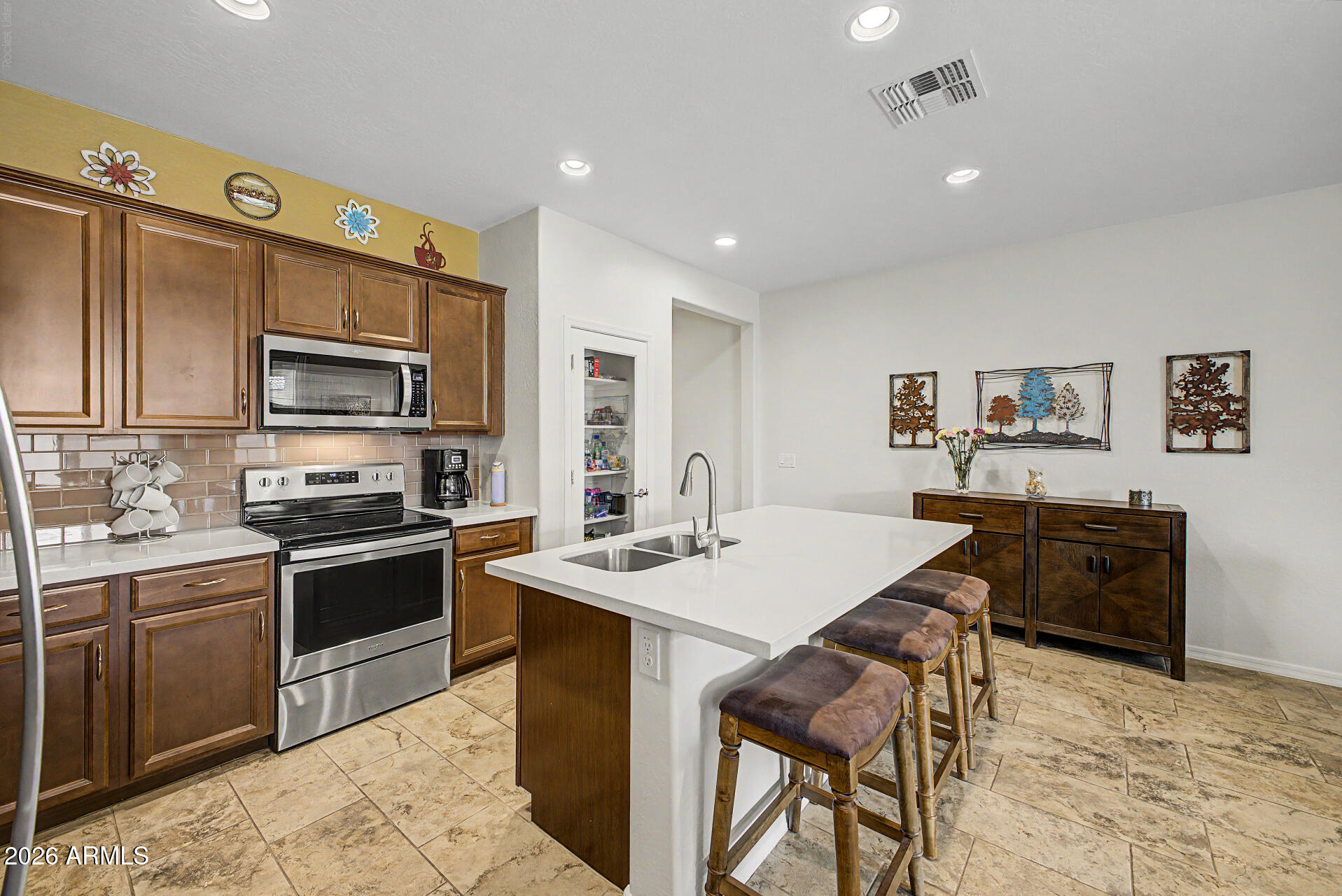 Meticulously maintained and move-in ready, this beautiful 2019-built home is nestled in a desirable gated community with convenient freeway access. Designed with today's lifestyle in mind, the open-concept floor plan features 9-foot ceilings, two full bathrooms, and a thoughtfully designed layout that maximizes both comfort and functionality. Step inside and be greeted by expansive tile flooring that flows seamlessly throughout the main living areas, complemented by plush carpeting in the bedrooms. The stunning kitchen is the heart of the home, showcasing a large island with breakfast bar seating, quartz countertops, designer tile backsplash, stainless steel appliances, recessed lighting, a brand-new refrigerator, and a fabulous walk-in pantry providing abundant storage. The split-bedroom floor plan offers privacy for the spacious primary suite, complete with a huge walk-in closet, dual-sink vanity, relaxing soaking tub, separate shower, and private water closet. The secondary bedroom and full bath are ideally positioned for guests or a home office. Enjoy Arizona living in the beautifully landscaped backyard featuring a covered patio, paver seating areas, colorful flowering plants, and a side gate for added convenience. The attached garage offers direct access to the home and includes overhead ceiling storage for extra organization. This exceptional home combines modern finishes, low-maintenance living, and an ideal location--everything you've been looking for in a gated community home.
