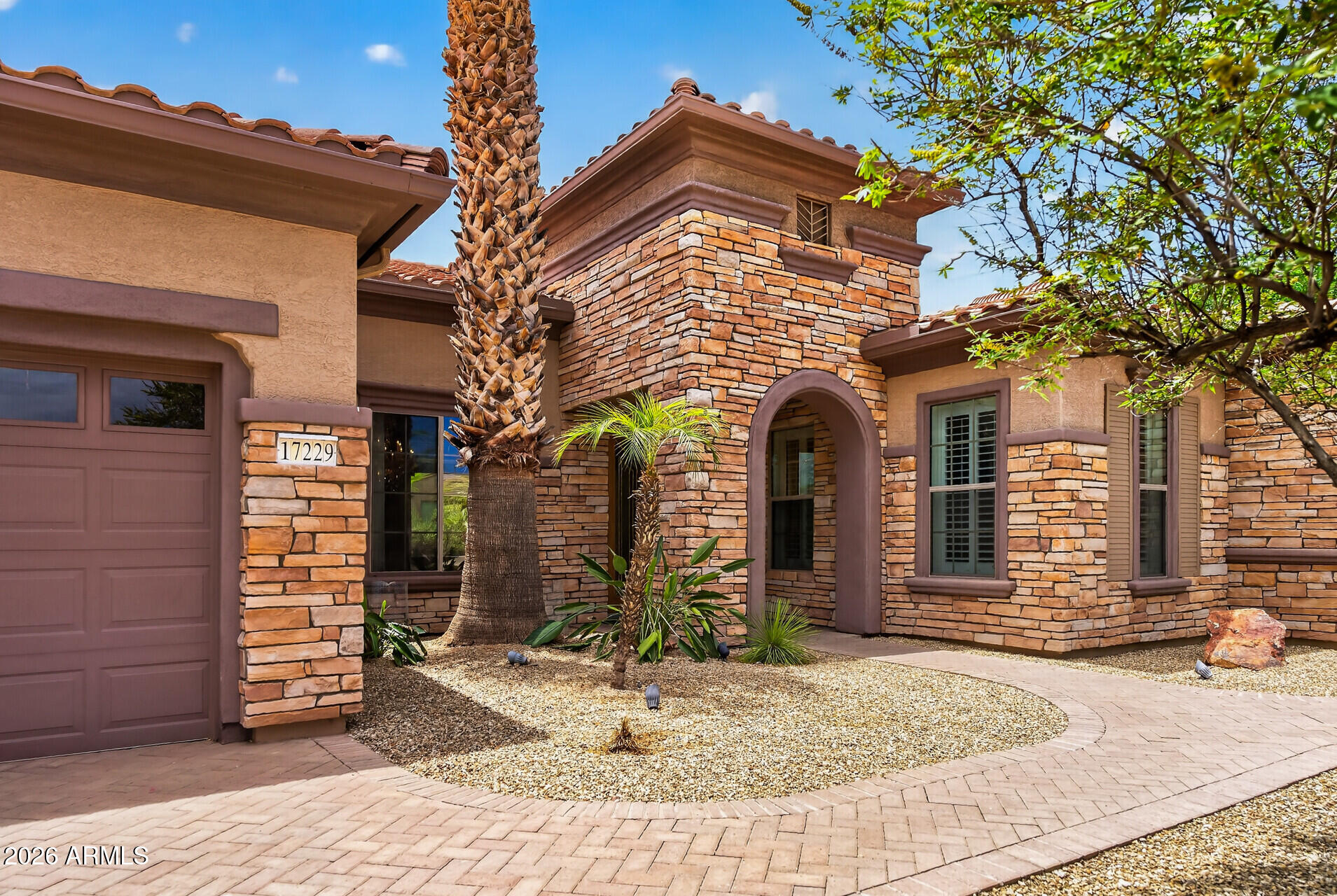 Welcome to The Manors, Grand's premier enclave of estate-sized homes known for its larger homesites, upscale architecture, and distinguished presence. First time on the market, this exceptional Windsor model encompasses 3,411 square feet and is perfectly positioned on a spacious 10,982 square foot corner lot. From the moment you arrive, the home's curb appeal sets it apart with an updated stacked stone façade, elegant portico entrance, leaded glass double doors, mature desert landscaping, and herringbone-pattern paver driveway and walkways. Inside, soaring 12-foot ceilings and an impressive marble entry create a grand first impression. Crystal chandeliers, crown molding, plantation shutters, bull-nosed corners, and oversized baseboards add timeless elegance throughout the home. Designed with both comfort and entertaining in mind, the split floorplan features three bedrooms, two and a half baths, and a two-car garage plus dedicated golf cart garage. The expansive primary suite offers a true retreat with room for a sitting area, while the spa-inspired bath features dual vanities, a soaking tub, oversized walk-in shower, and generous closet space.

The heart of the home is the spacious kitchen, showcasing granite countertops, stainless steel appliances, abundant warm wood cabinetry, a large center island with seating, and a sunny breakfast nook overlooking the backyard. The secondary bedrooms are thoughtfully separated from the primary suite, providing privacy for guests. One guest bedroom features a walk-in closet, while the third bedroom is currently configured as an executive office with custom dark wood built-in desk and shelving.

Additional highlights include a convenient powder room, large indoor laundry room with washer and dryer included, extensive storage cabinetry, utility sink, and two HVAC systems replaced in 2021.

Step outside to your own private resort-inspired retreat. The expansive covered patio features flagstone pavers, a tranquil rock waterfall fountain, and towering palm trees that create a lush tropical ambiance rarely found in the desert. Whether hosting guests or enjoying a quiet Arizona evening, this outdoor living space offers the perfect blend of privacy, elegance, and relaxation.
This is a rare opportunity to own a meticulously maintained estate home in one of Sun City Grand's most sought-after neighborhoods.