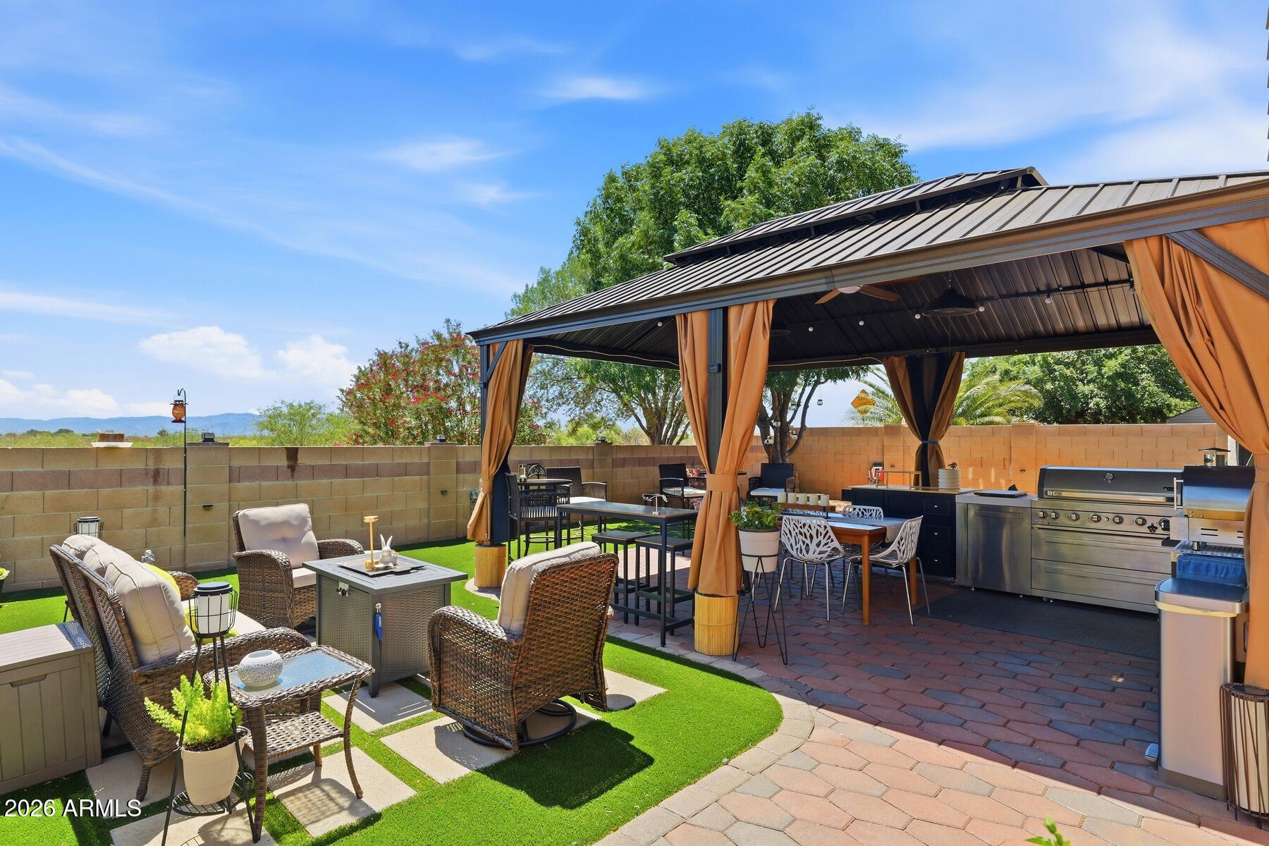 Exceptional indoor-outdoor living awaits in this beautifully designed home. Inside, the versatile open-concept floor plan is filled with natural light and enhanced by elegant, high-end finishes throughout. Granite countertops, abundant cabinetry, an electric fireplace, and custom tile flooring combine beauty with everyday comfort. Complementing the home's interior is an exceptional backyard retreat featuring a custom outdoor entertainment pavilion with kitchen, built-in grill, dining and lounge areas, ambient lighting, artificial turf, paver walkways, and mature landscaping. Enjoy open views and Arizona sunrises from this inviting retreat. Thoughtfully designed for comfortable living and entertaining, this exceptional property offers style and functionality throughout.
