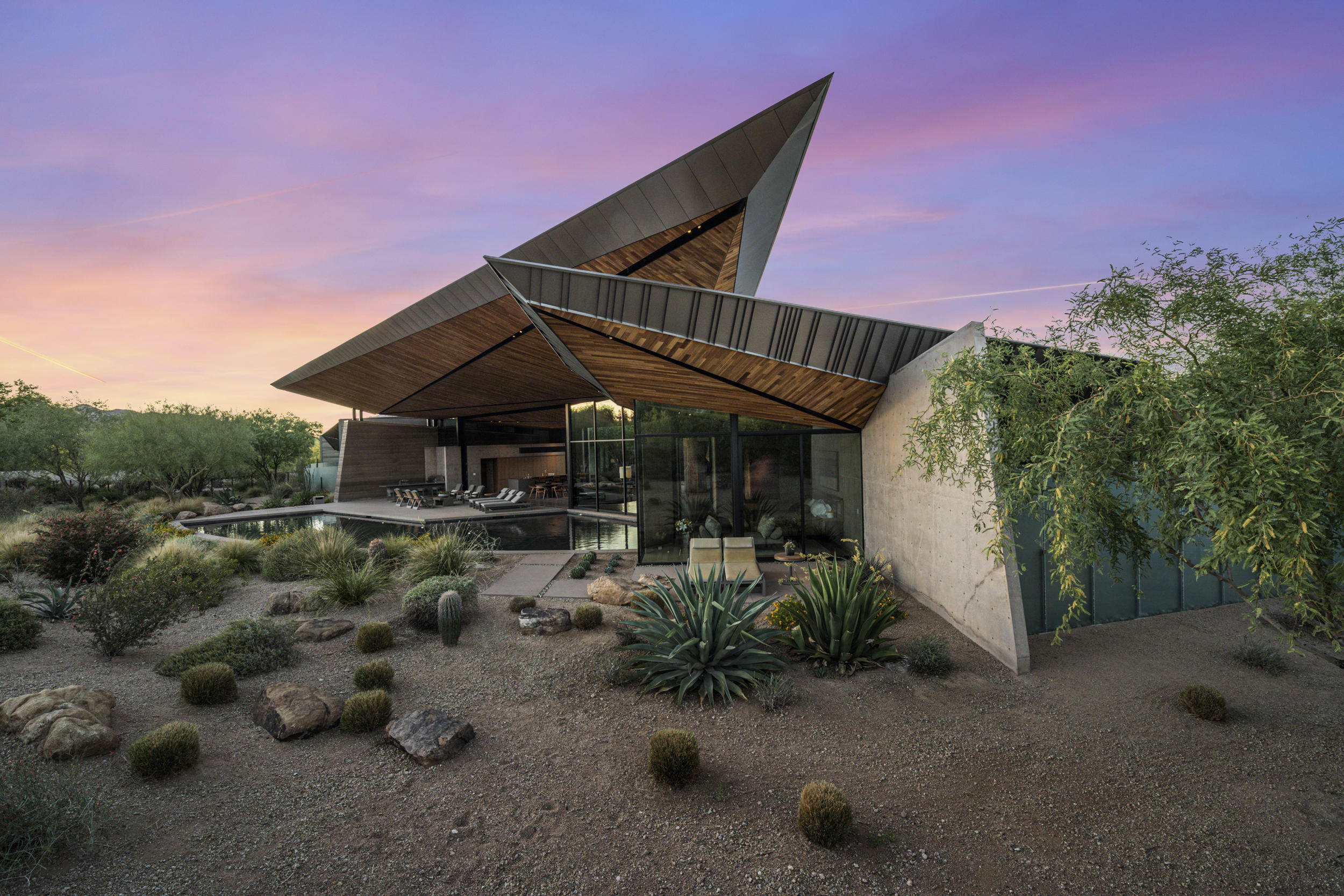 From what began as an appeal and vision to create the most alluring home in Arizona's highly sought-after Paradise Valley, Dancing Light came into being, a triumph in contemporary residential architecture that truly reflects the spirit of its natural surroundings. A sprawling 2.8 acres contains two stunning residences, with the main house and guest house consisting of 3 bedrooms and 3 ½ baths, and 1 bedroom and 1 bath, respectively. Prepare for moments of awe in this Kendle Design, Architect/Desert Star Construction/David Michael Miller, Interiors-designed 6,198 square-foot masterpiece replete with artfully functional details that extends naturally to the outdoors. Camelback Mountain is silently poised nearby, as if offering its blessing to a desert compound made up of the area's natural substances and the highest quality building materials. Enter through doors of frosted glass and be at once greeted by a sophisticated ambiance -  a desert courtyard surrounded by a comfortable, open living environment with views of the outdoors from almost any vantage point. Floor-to-ceiling sliding glass walls open up the great room into the exterior patio, eventually interrupted by soft wood panels and grey adobe-textured walls that frame the living spaces such as the ultra-modern kitchen, dining area, and wide hallways. Light streams in from well-placed windows, either at the floor, near the ceiling, or as accent walls, creating various nuanced shades in the spaces decorated by muted greys and light browns, with the occasional pops of color. The strategic placement of the pool affords cool breezes to the inside, and the roof appears as if it's rising up to meet the mountains. State-of-the-art features like Gaggenau appliances, Vola kitchen and bath fixtures, and custom woodwork fill the rooms, adding to the home's understated modern elegance. Powered by Savant technology, the entire estate can easily be controlled on-site or from a distance, whether it's maintaining the Gbtwo-meticulously designed landscape or engaging the home's security and energy systems. A stunning portrayal of domestic art, it is no wonder that the compound has caught the attention and acclaim of experts in architecture and design worldwide, being showcased in over 100 online design websites, mentioned in industry magazines and published books, and winning multiple home-building and design awards. With equally stunning views of the landscape, this home plus guest house is the perfect setting in entertainment or retreat for the most discerning of tastes.
