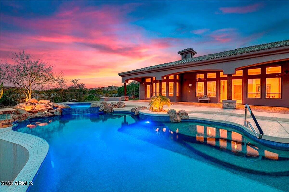 Tucked away on a quiet cul-de-sac in Estrella Mountain Ranch - The Trails, this extraordinary custom Jada home invites you to slow down, breathe deep, and take in the beauty of the desert. Set on over 1.1 acres and facing the majestic White Tank Mountains, this property offers a rare blend of privacy, craftsmanship, and sweeping mountain views that feel endless.

From the moment you step through the gated courtyard and hear the soft sound of the fountain, you know this home was designed with intention. Every finish reflects quality, from the rich travertine flooring and custom cabinetry to the Low-E argon gas windows and tankless water heater. Meticulously maintained, it is truly move-in ready.

The heart of the home is a chef's kitchen built to gather around -- featuring Viking appliances, a built-in espresso machine, an expansive island, and a separate walk-in pantry room. Whether hosting holidays in the formal dining room, enjoying quiet evenings in the great room, or working from the private den, every space feels both elegant and welcoming.

Movie nights become unforgettable in the dedicated media room complete with projector, screen, and surround sound. The fourth bedroom, with its own private courtyard entrance, offers the perfect setup for guests, multigenerational living, or a secluded office retreat.

Step outside and the experience only gets better. The resort-style backyard showcases an infinity-edge pool and spa perfectly positioned to capture glowing sunsets over the mountains. A pergola and outdoor BBQ area create the ultimate setting for entertaining under Arizona's sparkling night skies.

Living in Estrella means access to lakes, parks, trails, golf, tennis, and year-round community activities -- all while enjoying the serenity of desert living with convenient access to Phoenix and Palo Verde.

This is more than a home. It's a private desert retreat where quality meets lifestyle, and where every sunset feels like it was painted just for you.