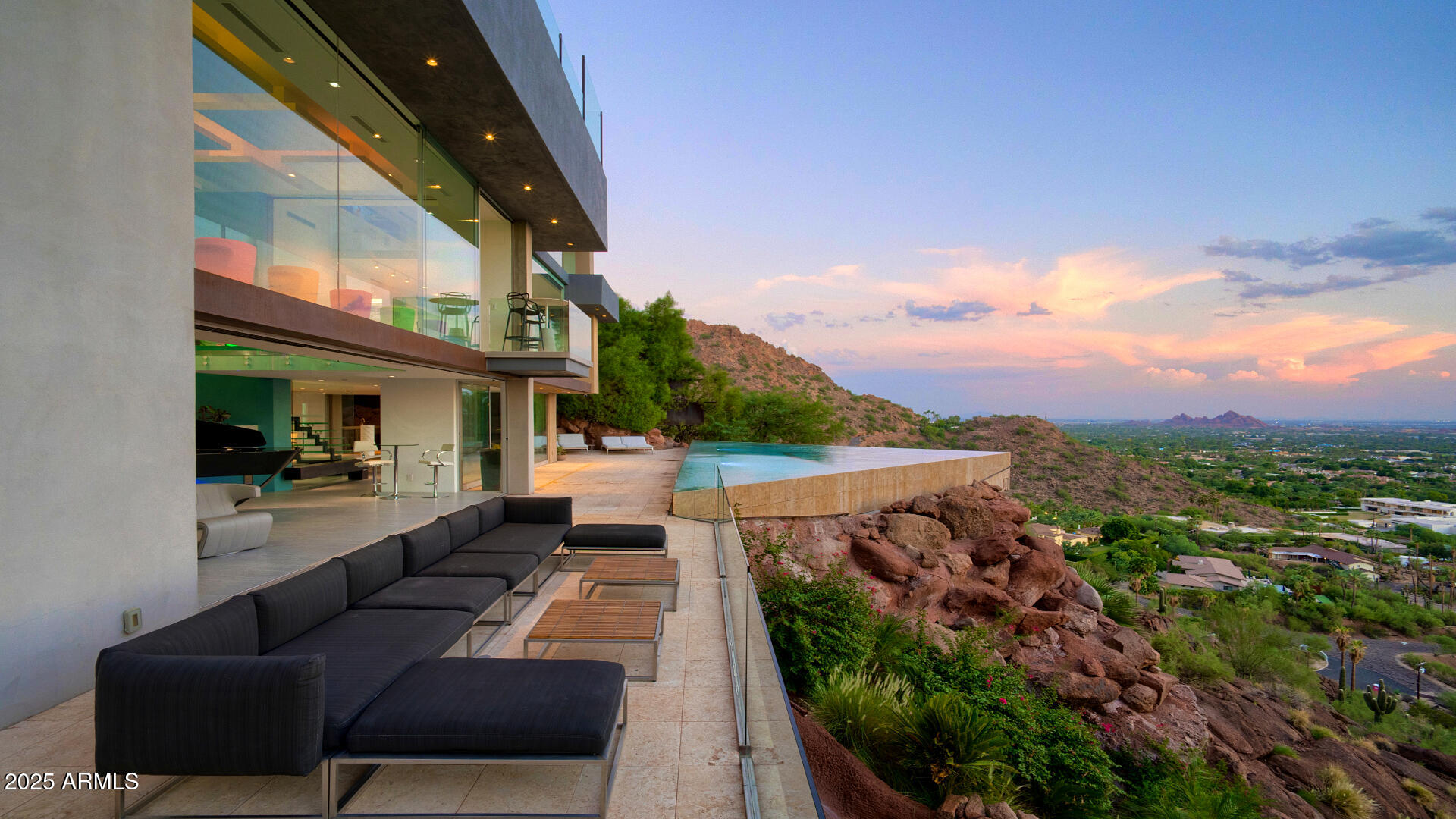 Come experience this breathtaking hillside home. Red Rocks of Camelback provide a backdrop for the extraordinary architecture with elements that blend beautifully into the scenery and elements that provide exceptional juxtaposition with contemporary flair. Views are panoramic, and luxury finishes and furnishings are over the top. Just a few of the incredible features include the infinity edge pool, cantilevered guest house, in-house bar with frozen rail, game room with red rock climbing wall, rooftop seating and fire features, tiered putting greens and several massive waterfalls.  Epic is just the beginning.