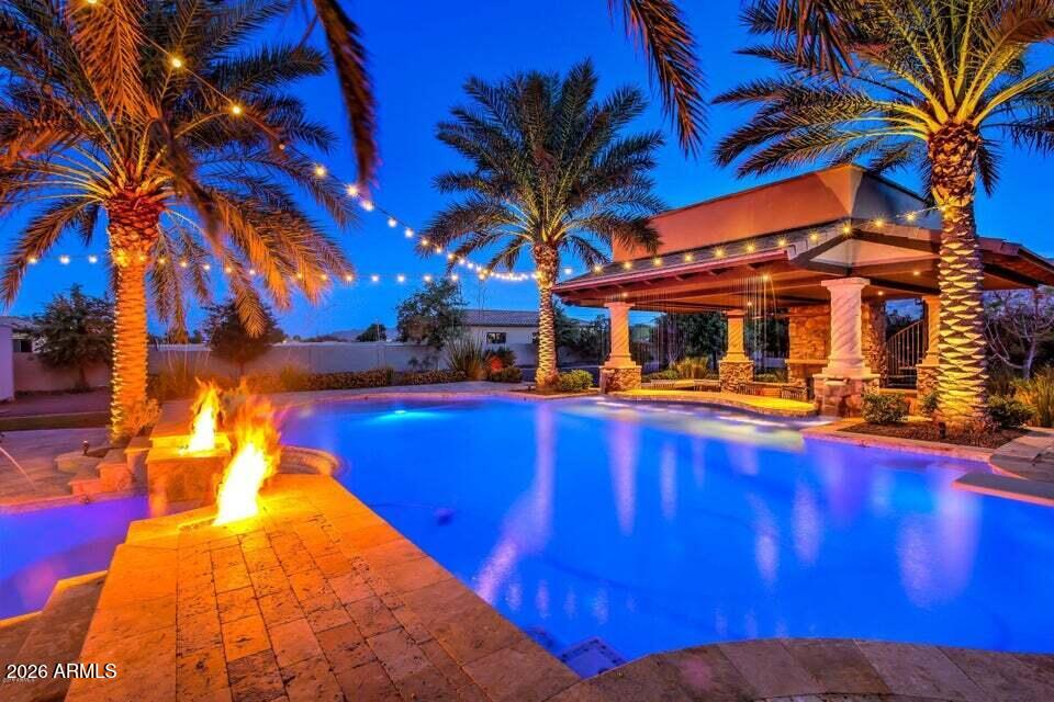BEST HOME ON TOUR ''BEST PRESENTATION & VALUE''!! This unique custom estate has a QC mailing address but is actually located within the TOWN OF GILBERT offering a highly desired location, fantastic amenities of GILBERT and highly ranked A+ Chandler schools! This gorgeous custom home sits on a private 1.2 acre lot with no HOA and horse privileges, offering breathtaking mountain views and the ultimate in privacy! Professionally designed outdoor living spaces, creating a truly spectacular backyard retreat that feels like your own private resort! The resort-style pool design gives The Phoenician & Biltmore a run for their money! 2 POOLS...yes 2! An elevated diving pool with a negative edge, spills over into the lower play pool below.  (continued...) The upper pool features a swim-up bar with seating for 7, perfectly positioned to enjoy the amenities of the stunning 2-story ramada. Designed with entertaining in mind, the lower level of the ramada offers multiple lounge areas, including a cozy seating area centered around one of two fireplaces. A spiral staircase leads to the upper viewing deck, where another fireplace and sweeping views of the San Tan Mountains create a spectacular setting for relaxing evenings and unforgettable sunsets. Every detail of the backyard was thoughtfully curated--from the expansive patio just off the home featuring a built-in BBQ area, elegant bar and beverage center with custom shelving, LED lighting, and kegerator, to the abundant custom seating areas throughout the space. Enjoy your favorite music through two-channel surround sound while staying cool beneath the industrial ceiling fan. This outdoor living environment truly redefines luxury entertaining. Inside, the home is equally impressive. Meticulously maintained and highly upgraded, the thoughtfully designed floor plan features two primary suites on the main level, along with a beautiful executive office. The fully finished basement offers two spacious bedrooms--each with walk-in closets and private patio access--as well as a kitchen, laundry room, and a comfortable living room that opens to an additional outdoor patio, creating an ideal space for guests or multi-generational living. Throughout the home you will find rich wood and travertine flooring, custom window treatments, upgraded cabinetry, matching built-ins, designer lighting, and soaring ceilings that enhance the home's elegant character. The chef's kitchen is designed to impress, featuring an oversized induction cooktop, upgraded stainless steel appliances, an expansive center island, a massive walk-in pantry, and beautiful granite countertops. Additional custom details include alder wood doors, smooth wall finishes, and kerfing throughout, reflecting the exceptional craftsmanship found throughout the home. Car enthusiasts and RV owners will appreciate an oversized 3-car garage, gated 8-car auto court, and two RV gates--including an automatic front gate and a rear gate providing full access to the backyard. Conveniently located just minutes from shopping, dining, and entertainment at SanTan Village, as well as Gilbert's 272-acre Regional Park and easy access to the Loop 202 freeway. 
This meticulously maintained, highly upgraded estate offers a rare combination of luxury, privacy, and resort-style living--an extraordinary opportunity to truly live in your own PARADISE!
