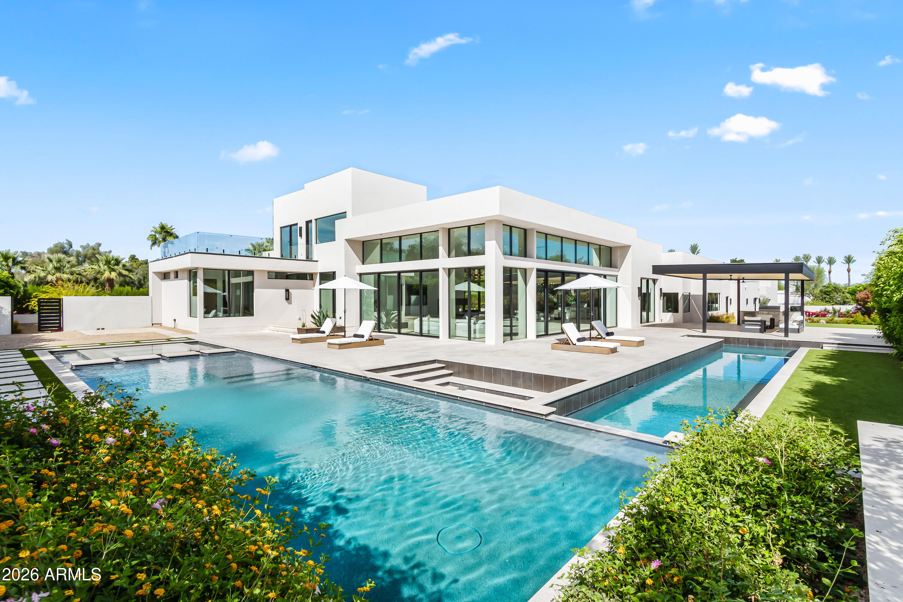 Positioned along one of Paradise Valley's most prestigious enclaves, this privately gated 1.1-acre estate showcases uninterrupted panoramic views of Camelback Mountain, including the iconic Praying Monk. Designed to maximize natural light, volume, and seamless indoor-outdoor living, the residence offers a refined blend of modern elegance and resort-style amenities. The main home features five spacious bedrooms, 5.5 bathrooms, and a versatile bonus room ideal for a home office, gym, or studio. A detached guest house provides two bedrooms, 2.5 bathrooms, a full kitchen, and private laundry--perfect for extended stays or hosting with complete independence. Inside, soaring ceilings, expansive walls of glass, and wide-plank oak flooring create a bright, open atmosphere. The great room serves as the centerpiece, highlighted by dramatic sliding glass doors and a sleek marble fireplace, effortlessly connecting to the outdoor living spaces. The open-concept kitchen, dining, and living areas are designed for both everyday living and elevated entertaining. The chef's kitchen is equipped with premium Wolf and Sub-Zero appliances, a gas range, dual ovens and dishwashers, built-in coffee and ice makers, and a striking climate-controlled wine wall. The primary suite offers a serene retreat with tranquil views and private access to the backyard, along with a spa-inspired bathroom featuring a sculptural stone soaking tub, oversized steam shower, dual vanities, custom wood cabinetry with abundant storage, and a private water closet. Outdoors, the showstopping custom pool and spa include an extended lap lane, surrounded by multiple lounging and dining areas, fire features, and a covered steel-and-wood patio with a fully equipped outdoor kitchen. Added amenities include a pickleball court and putting green. Additional highlights include a six-car garage and a prime location just minutes from Arizona's premier resorts, spas, fine dining, and shopping.