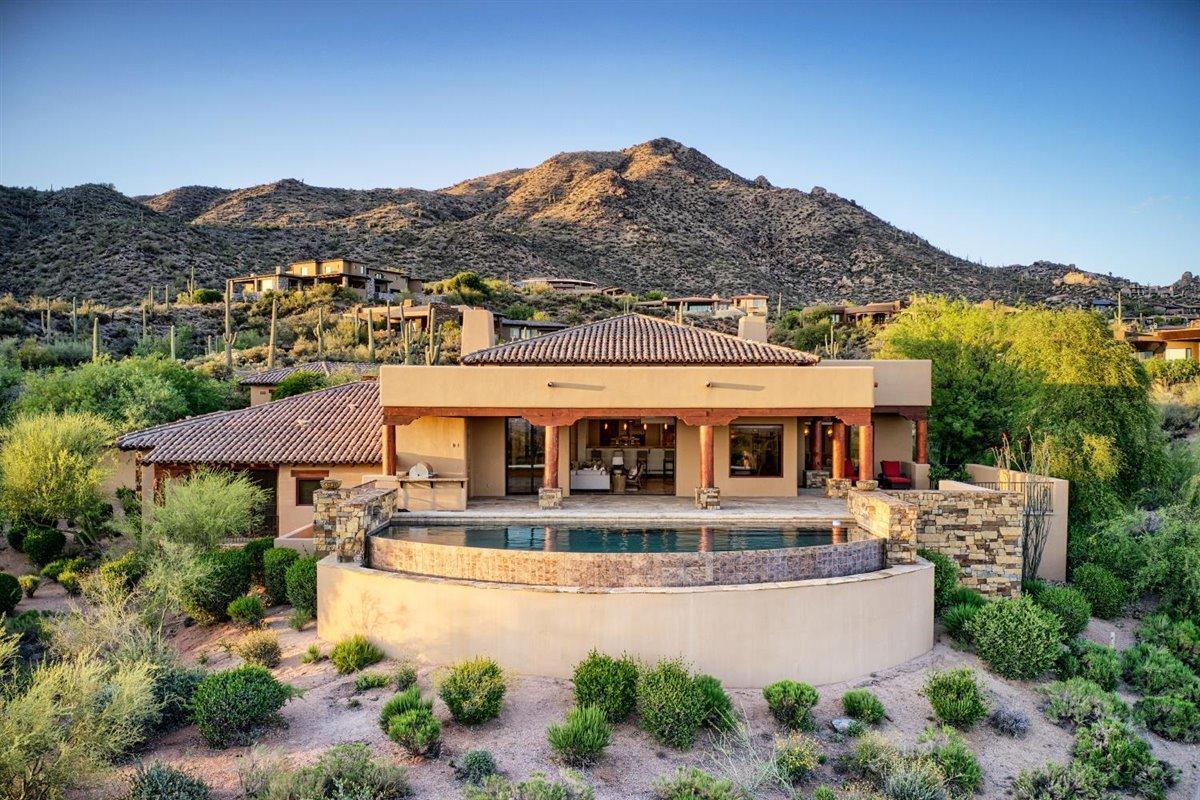 Welcome to Seven Arrows 23, a 5,724 s. f., ''light and bright'', south-facing, open ''Great Room'' plan home, custom-designed for its 42,207 square-foot site, in a ''Desert Southwest'' architectural style, in Desert Mountain, an 8,200 acre, thirty-four-year-old, master planned community in north Scottsdale, AZ, with a nationally prominent, membership optional, private club within its gates.  Built in 2005, the Main House (which measures 4,883 square feet) has four ensuite bedrooms (one set up as an office), a Powder Room, and a Pool Bath.  There is also a separate two-room Casita (which measures 841 square feet), with a living area/kitchenette in addition to a bedroom and a double-lavatory bathroom. The Main House has an oversized "three-cars plus" garage; a 38' wide negative edge play pool; a spa; and a large, sunny back patio with a lot of shade and a 32" wide, built-in barbeque with sink. The landscaping is mature and plentiful. 

Main views, to the south, include the McDowell Mountains (and iconic Pinnacle Peak) about seven miles away; a vast, twinkling carpet of city lights by night about twenty-eight miles away, and great sunset views" in winter, spring, and fall.  There is a small golf course grass view.  A sixty-yard-wide view corridor across the street to the west is guaranteed, thanks to the existence of a golf course easement.   

The home is on an elevated cul-de-sac in one of Desert Mountain's highest "Villages" with only thirteen homes beyond it, so traffic is light.  Busy roads are out of earshot, so the location is quiet, especially on the back patio at sunset when you might be there enjoying a beverage.  This home is a wonderful place to relax, get refreshed, rejuvenated, and reacquainted, with oneself, one's spouse and children, or good friends in for a few days as house guests.  It is a wonderful home with remarkable surroundings and experiences waiting at every turn.   

In addition to the views, which are largely fixed, many other details make this home special including: a Wine Room (traditional racking for approximately 500 bottles); Lutron lighting controls; three fireplaces (Great Room, Master Bedroom, and the Front Porch); a Massage or Storage room (which do you need more?); some relatively recent upgrades including two gorgeous glass and iron doors (for the house and the casita); two water heaters (one conventional; one a Navien tankless); sliding, stacking doors across the width of the Great Room; and one HVAC unit (out of four); several lighted art niches; stone baseboards throughout; raised hearths and mantels on the two indoor fireplaces; a separate, out-of-the-garage storage place for two dumpsters; and, off-street parking for four cars. 

The garage has two doors, at two different angles, creating extra garage space for a small- to medium sized car (or bicycles, motorcycles, etc..); three 10' wide storage cabinets; a hose bib; a wireless remote door entry; a dog washing station; natural lighting thanks to five windows; and epoxy floor coating.  Nominally big enough for three cars, the extra "wedge" of floor space could easily make this a four-car garage. 

The Master Suite is large and includes a large stone fireplace with raised hearth and mantle; carpeting in the bedroom; double vanities; a makeup counter; double closets, double toilet rooms (one with bidet); a four-head, steam shower; and a carpeted Exercise Room (partially covered with twenty-four 24" square thick rubber interlocking floor mats to protect against dropped weights); an overhead TV; a counter and drawers, and a place under the counter for a refrigerator.  

The Kitchen is a well-equipped "working kitchen"  with 37" high counters, a large, rectangular center island (raised at one end to create dining space for two); a Wolf six-burner plus a griddle gas range top with a pot-filler and two ovens below; two GE dishwashers; a 25" Kitchen Aid Convection oven and a warming drawer; granite countertops; a 13' 7" wide Breakfast Bar (perfect for serving meals to deserving adult visitors or Grandkids); two sinks; and a built-in Miele coffee center.  Views are from an elevated vantage point (two steps above the Great Room) over the Breakfast Bar into and through the Great Room of the pool and the McDowell Mountains and city lights beyond.  A large Butler's Pantry off the Kitchen offers abundant storage.  

The Great Room has a generous seating area; space for a "formal" dining room table under a very nice chandelier; a high, wooden, tongue-in-groove ceiling system with large square beams; a built-in entertainment center housing a 56" (diagonal) Samsung television and a sub-woofer; surround sound; sliding glass doors; and easy access to the Wine Storage room.  

The two-room Casita (a big bedroom with a walk-in closet, and a living/dining area with a raised counter with seating for two bar stools) has an under-counter U-Line refrigerator with an ice maker, and a GE dishwasher and microwave.  One of the separately available televisions (a desktop 49" (diagonal) Samsung) is in the living area.  Washer and dryer hookups are in a closet. 


The southwest solar exposure allows for lots of back patio sun until late in the afternoon, but shade when the sun is low in the sky or during our warmer summer months, making the back patio very useful as a place to relax without having to fight the setting sun every night, colorful sunset or not.   

Golf is a "big deal" at Desert Mountain, and full golf Members enjoy six Jack Nicklaus-designed championship golf courses; one par-54 course with eighteen par-3s, four practice ranges; and a high-tech teaching and club-fitting facility.  Other on-property outdoor recreation opportunities, for all Members include tennis, hiking, swimming, bocce, pickleball, horseback riding, and croquet. 

Seven clubhouses serve the needs of the Members, including the Sonoran Clubhouse, a truly amazing swim (three pools), tennis (nine courts, including one grass, five Har-Tru, and three cushioned surface hard courts), fitness, and spa facility with a grill restaurant.  It enjoyed a $12,000,000 renovation in 2016. The following summer saw six pickleball courts, two bocce ball courts, and a croquet court added. It is now perhaps the premier facility of its type in the Southwest.  The Club's nine dining venues offer a wide variety of food, wine, and atmospheres. No coats and ties required! The Club's membership is catered to relentlessly by an attentive staff and Concierge, providing unparalleled service.  The place is "phenomenal", so good, three multi-million-dollar lottery winners have chosen Desert Mountain as the place they want to live.

As mentioned, membership in the Club is optional, but since the Club is the emotional, physical, and social "core" of the place, the opportunity to be a member of the Club is a significant part of the attraction of living in Desert Mountain for most property owners.  Several membership programs exist, available subject to supply and demand and upon successful application to the Club.  The Club is very highly regarded within the world of Private Clubs, and there is an ambitious plan in place to update all the Club's major facilities over the next few years in order to provide an even better experience for its Members.   

Desert Mountain's over 1,900 homes are spread out in over forty "Villages".  Seven Arrows is highly regarded due to it being of the four highest Villages, and one of the most intimate, with only thirty-two properties.       

Desert Mountain is on the slopes of the Continental Mountain range on the northern edge of Scottsdale, contiguous to the fourth largest National Forest in the country. There is a twenty-mile private trail system in these mountains for exclusive use of Desert Mountain residents.   The top elevation is 4,890', highest in all of Maricopa County, affording dramatic views.  Phoenix Sky Harbor Airport is about a forty-minute drive from the community's Front Gate.  

Desert Mountain is a place of surpassing scenic beauty with long-range, panoramic views of Phoenix, Scottsdale, the entire "Valley of the Sun", many mountain ranges near and far, and, of course, Arizona's famous sunrises and sunsets! It now has just over 1,900 finished homes ranging in size from 1,800 to over 20,000 square feet with listed properties ranging in price from about $1,300,000 to $16,500,000. Owners have invested over $30,000,000 in individual homes. It has attracted full-and part-time residents from all over North America, Great Britain, and western Europe. Another steady attraction are real estate taxes that are strikingly low compared to many parts of the country, particularly the Northeast, Midwest, and California. (the 2020 taxes on this home were only $9,240.54).  The weather is famously sunny, and our risk of natural disasters is extremely low. Being higher and somewhat removed from the city means the stars are bright at night and the air is typically much cleaner than what lies over the Valley. For you readers thinking Arizona is too hot in the summer to enjoy year 'round living, this home is at an elevation of about 3,260' making for a fabulous climate twelve-months of the year, given the lack of humidity and the way the desert loses its heat when the sun goes down in the summer.  

Relative to more local locational concerns, day-to-day shopping needs for Desert Mountain owners are well-handled within about a ten-minute drive by the merchants in the nearby towns of Carefree and Cave Creek. There are approximately 69 restaurants and bars within about sixteen minutes' drive of Desert Mountain's Front Gate. The Phoenix/Scottsdale area is famous for world-class shopping, major league and collegiate sports, terrific air service (Phoenix Sky Harbor Airport is routinely less than a forty-minute drive from the Front Gate), and a wide variety of cultural attractions.  Desert Mountain is within two and a half hours of normally excellent snow skiing in Flagstaff. Its location in the southwestern part of the United States affords easy access by air or car to the entire American West, with especially easy access to San Diego, Los Angeles, Las Vegas, the Grand Canyon, Lake Powell, and a plethora of unbelievably beautiful places in Southern Utah. "Paradise" does not overstate it.  Scottsdale is also famous for great medical care, with a Mayo Clinic and a separate Mayo Hospital.  

Thanks for your interest in this home. Against this backdrop of privacy, service, beauty and recreation, Seven Arrows 23 represents an unusually nice opportunity and value. We look forward to showing it to you someday and helping you learn about the community, the Club, and the area!