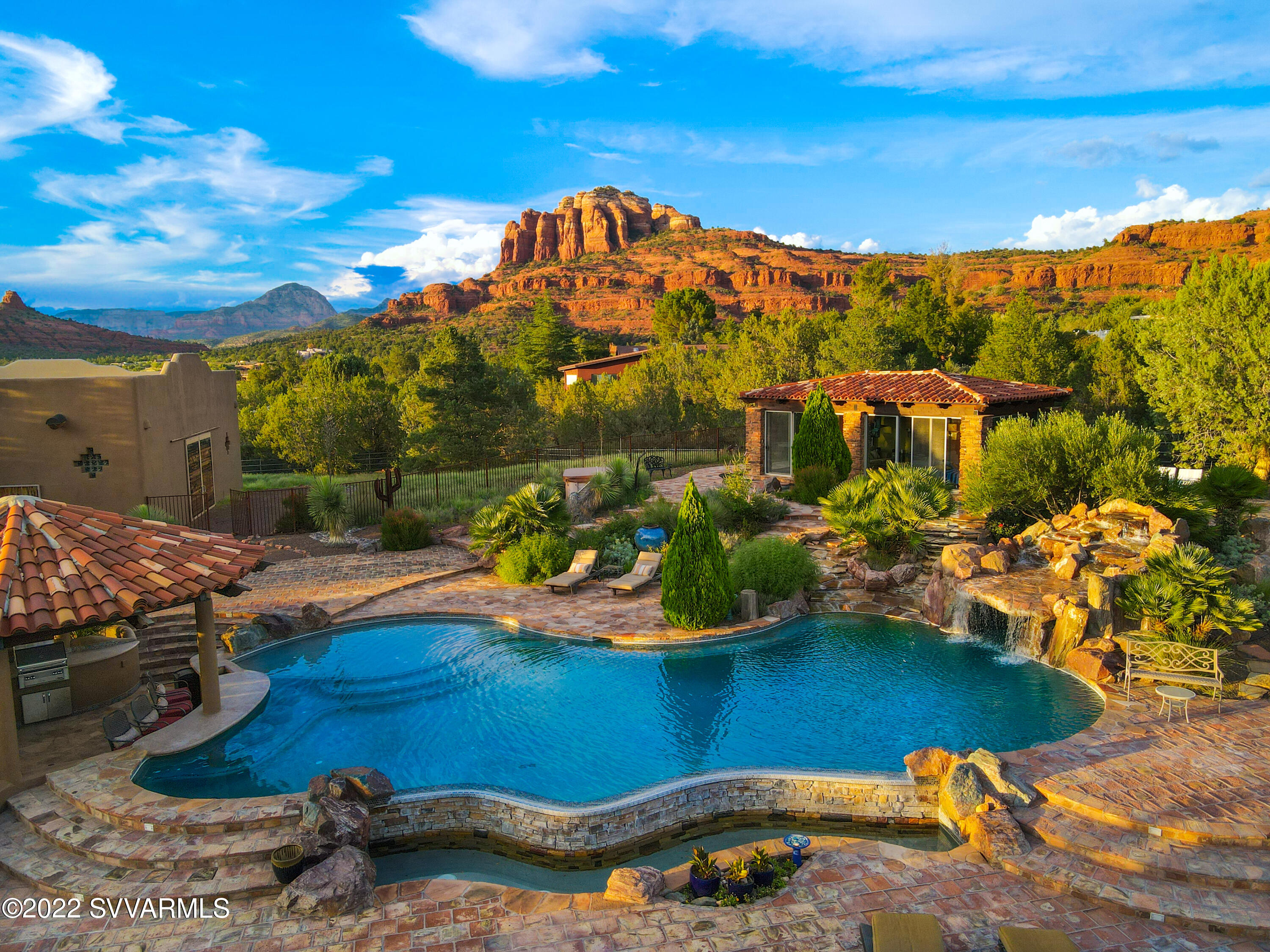 This property is like no other - as rare and unique as a white buffalo in the American Southwest with healing properties all of its own, a one of a kind sensational luxury resort, a portal to a peaceful place of sublime beauty, an entertainer's playground, a family compound with a luxury horse facility.  Your very own sanctuary nestled beneath big panoramic views of the world famous Cathedral Rock and Seven Warriors awaits!  The gorgeous single level 4100 SF Santa Fe/Pueblo style home on 2.28 acres features 2 Owner's Suites, 5 fireplaces and large wood viga beams, with curved walls creating both warmth and flow throughout. The property is on a double gated private road. Enjoy Sedona's highly desirable indoor/outdoor lifestyle at your very own private oasis with a large state of the art salt water negative edge pool.   Hear the sensuous, soothing sounds of cascading waterfalls filling your backyard against the desert sky. There is even a unique Hefner Style Grotto above the main pool which seats 6!  How about some morning yoga in the floating Ramada surrounded by a gentle flowing river?  Or follow your creativity and utilize the Ramada as an art studio during the day, turn it into a movie theatre in the evening or just enjoy the magical sunsets.  Did you see the fully equipped sunken outdoor kitchen with a swim up bar and baja step for hot summer nights? Don't forget the garaged parking for up to 9 cars and toys.  If you have horses, they will enjoy the oversized stalls in the state of the art stable with overhead misters and video monitoring, or convert the stable into additional garaged parking for your luxury vehicles and toys.  A guest casita/caretaker's quarters/studio apartment is attached to the stable, a separate hay barn offers storage and more garaged parking. This unique luxury estate features a total of 5,381 SF of livable area, 4 bedrooms with a bonus office/5th bedroom and a total of 11,281 SF under roof - it is truly an entertainer's dream, peaceful and serene healing sanctuary adjacent to 100s of miles of USFS trails right at your doorstep to enjoy the expansive magnificent nature of Sedona!  Construction of Integrated Concrete Form with 13" thick walls and in-floor hydronic heating ensures your comfort and will keep your energy bills low.  This property oozes owners pride, it is in great condition and move-in ready!  Ask for the extensive list of improvements since last purchase.