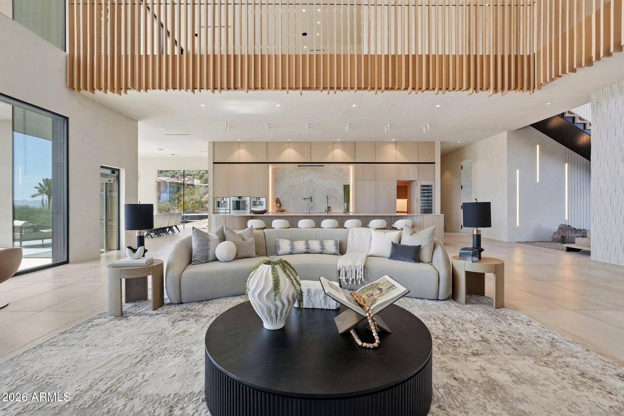 At the base of Camelback Mountain on the coveted south slope, this exceptional contemporary estate captures sweeping city-light and mountain views while delivering a rare blend of architectural drama, resort-caliber amenities, and effortless indoor-outdoor living.
The experience begins long before the front door. As you ascend the driveway, a carefully curated landscape composition and striking architectural silhouette create an immediate sense of bespoke living. Layers of glass, stone, and sculptural design elements intertwine to evoke intrigue, setting the stage for what lies beyond.A grand 10-foot by 9-foot pivot entry door reveals a breathtaking double-height foyer and great room, where soaring ceilings continue and are highlighted by LED chandelier, a living planter feature wall, seamless flush-mount switches, and artisan lime-wash walls establish a sophisticated yet tranquil aesthetic. Expansive collapsible walls of glass dissolve, opening to a covered terrace complete with a built-in BBQ and sink, all overlooking the pool and spa that appear to merge with the city skyline beyond. Thoughtful modern conveniences include an elevator, prewiring for whole-home audio, a Lutron lighting control system, Awake windows and doors, and a beautifully appointed laundry room featuring stackable machines, a utility sink, and a dedicated dog wash station.
Designed equally for elevated entertaining and everyday living, the kitchen is anchored by a dramatic 26-foot island with integrated wireless charging, that serves as both a gathering place and architectural centerpiece. Hidden beyond, a fully equipped back kitchen allows for effortless preparation and service. An exceptional suite of Gaggenau appliances includes steam ovens, an espresso station, and gas range with teppanyaki. The formal dining area blends innovation with refinement. Nearby, a statement powder room showcases a floating wall-to-wall vanity positioned before a floor-to-ceiling picture window, creating a design moment guests will not soon forget.
Ascend the sculptural floating staircase or take the private elevator to the upper level, where a versatile loft serves as an ideal retreat for entertaining or everyday relaxation. Complete with a wet bar, beverage refrigerator, wine fridge, ice maker, and custom backsplash, the space extends effortlessly onto a covered wraparound balcony anchored by a fireplace and panoramic views. Ensuite guest accommodations provide privacy and comfort, while two dedicated office spaces offer flexibility for any lifestyle.
The primary retreat is a sanctuary of wellness and serenity, offering direct access to both a covered patio and private balcony, each positioned to capture unforgettable city and mountain vistas through floor-to-ceiling pocketing glass doors. The private wellness retreat bath is designed around restoration and rejuvenation, featuring a sauna, cold plunge, floating double vanities, a freestanding concrete soaking tub, and a luxurious wet room with both a flush-mount rain shower and steam shower. Dual oversized walk-in wardrobes, including one with stacked laundry, and separate private water closets with wall-mounted fixtures complete this extraordinary suite.
Connected by an architectural bridge, the detached casita offers remarkable flexibility for guests, multigenerational living, wellness pursuits, or extended stays. The space features a private bedroom with ensuite, additional half bath, stackable laundry, a fully equipped kitchen with cooktop, hidden ventilation, steam oven, refrigerator, and dishwasher, as well as a dedicated gym area. Floor-to-ceiling window walls, a wraparound deck, and a private patio create a living experience that feels both connected to and independent while staying luxurious.
Rarely does a home so successfully unite visionary design, cutting-edge technology, and resort-inspired living. Framed by the iconic backdrop of Camelback Mountain and immersed in panoramic city views, this is more than a residence, it is a statement of architecture, lifestyle, and modern luxury at its highest expression.