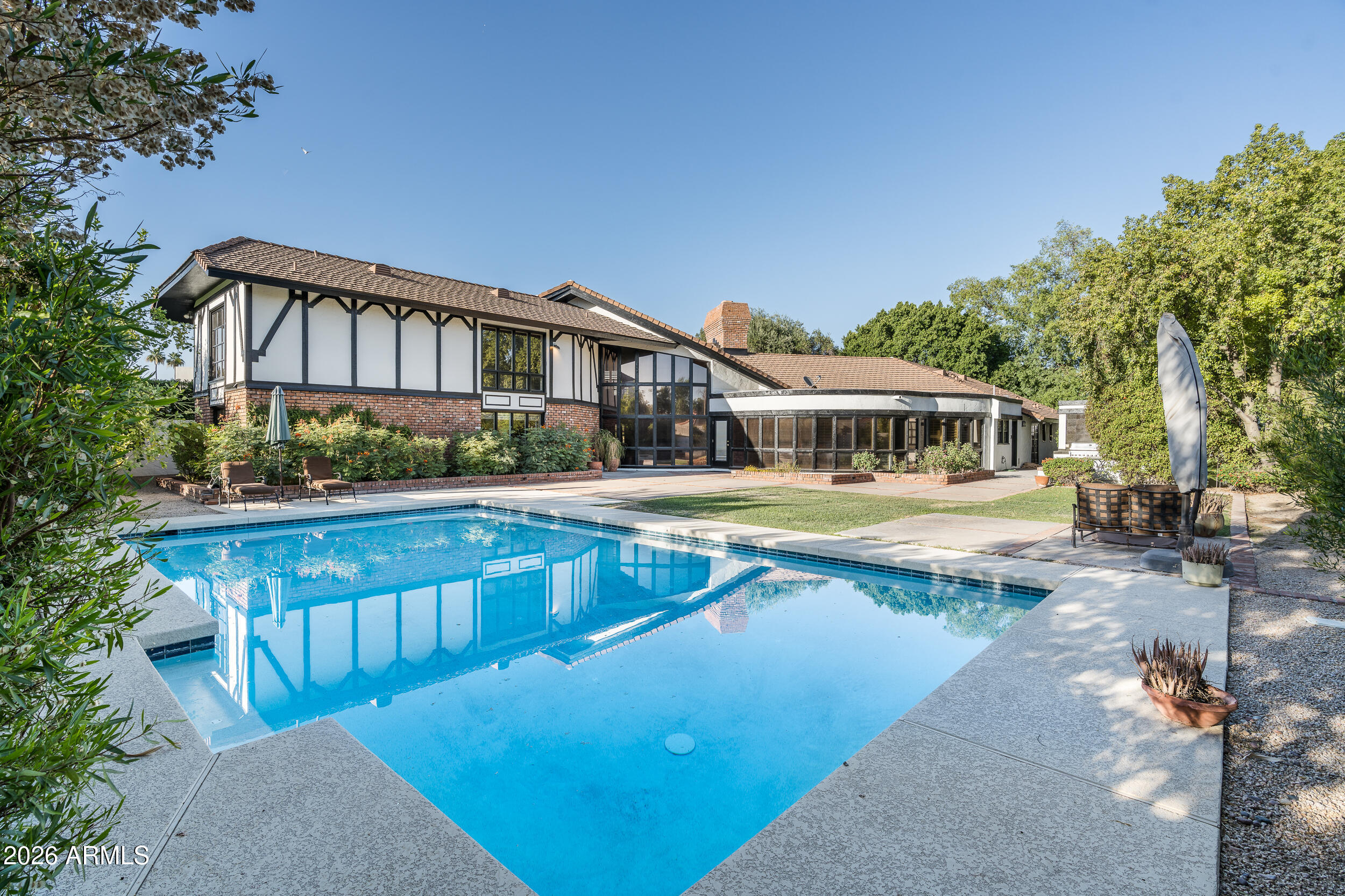 Compelling opportunity in one of Phoenix's most coveted neighborhoods--where renovated homes are commanding significant premiums. This custom-built English Tudor presents a rare chance to secure scale, character, and location with immediate livability and clear upside.
Originally constructed in 1979, this 5 bed /5 bath residence offers architectural integrity and square footage that would be cost-prohibitive to replicate today. Rich walnut floors with brass peg detailing, leaded glass entry doors, a grand staircase, and a French crystal chandelier establish a timeless foundation ready to be reimagined or enhanced.
Floor-to-ceiling windows bring in natural light, while multiple living and entertaining spaces--including a curved-glass formal dining room, expansive family room with stone fireplace, and upstairs loft with herringbone brick fireplace--create strong bones for a high-impact renovation.
Situated on a mature, landscaped lot with pool, this property is ideally positioned for a strategic refresh or full-scale transformation, capitalizing on the strong resale potential within Madison Meadows and the surrounding central corridor.