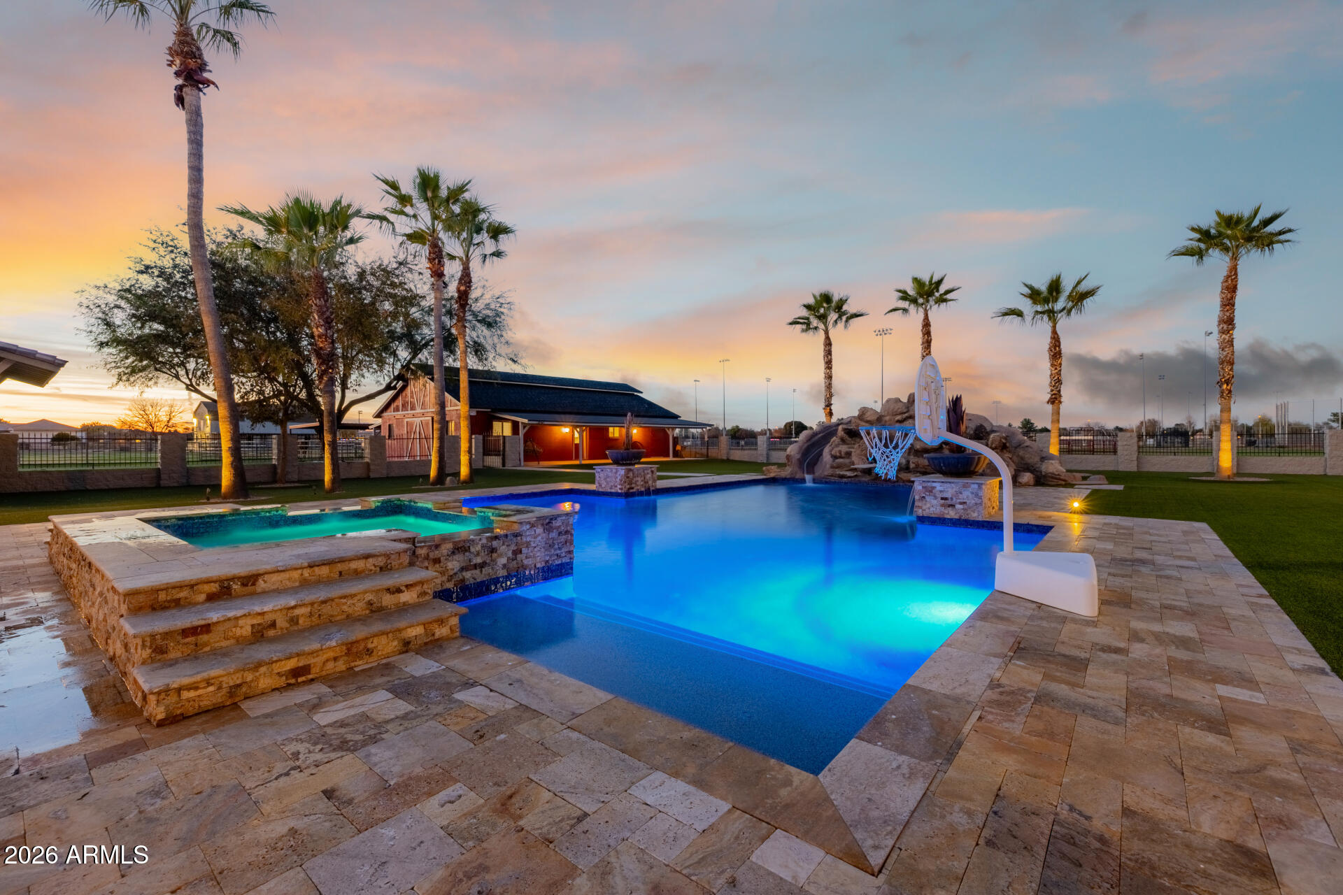 If you've been dreaming of a place where every day feels like a getaway, this exceptional estate delivers. Situated in one of Gilbert's most sought-after areas, this quiet and private property spans nearly 5 irrigated acres, an offering that rarely comes to market. The seller invested extraordinary care into the home, sparing no expense and thoughtfully upgrading every detail throughout. The custom single-level main residence of almost 6,600 sqft. offers 5 beds, 4 beautifully tiled natural stone baths, 2 laundry rooms, plus spacious bonus room that could easily function as a 6th bedroom with exterior access. Guest house! One of the home's most impressive features is the expansive 1,250 sqft. game room, showcasing vaulted wood-beam ceilings, a stone fireplace, a built-in dining table and a custom oak wraparound bar and ideal setting for entertaining. Multiple doors open to the backyard, creating seamless indoor-outdoor living.The great room flows effortlessly into the gourmet kitchen, which is equipped with newer dual dishwashers, a wood-front Sub-Zero refrigerators, high-end stainless-steel appliances, a built-in Sonic-style ice maker, a large granite slab island, and a six-seat breakfast bar. The primary suite serves as a private retreat, featuring a spa-inspired jetted soaking tub, steam shower, rain shower, bidet, separate sitting area, and direct access to the backyard oasis. Throughout the home, you'll find travertine tile, ¾-inch hardwood, engineered wood flooring, and carpet in two bedrooms. Custom solid alder wood cabinetry adds warmth and craftsmanship throughout. In addition to the main home, the property includes a 650 sqft. guest/pool house perfect for guests or multi-generational living with a full kitchen, laundry room, and bathroom with tiled shower. The estate offers an attached two-car garage as well as a detached workshop/garage with space for two oversized vehicles. RV hookups are available at both garages, along with a Tesla charger and upgraded 600-amp electrical service at the main home, making it solar-ready. Designed for both relaxation and entertainment, the resort-style backyard features a 45,000+ gallon heated pool with a waterslide and diving board, an eight-person spa, artificial turf, a two-way fireplace, and a large outdoor kitchen with seating for twelve, a gas grill, coolers, and sink. For equestrian or outdoor enthusiasts, the property also includes a pasture, large riding arena, round pen, barn, covered hay storage, and four covered horse stalls. A lighted sport court with speakers accommodates basketball, volleyball, tennis, pickleball, and more. Recent improvements include new exterior paint, a new barn roof, refreshed front and back landscaping with pavers and new rock, water softeners for both residences, upgraded attic insulation, and a new concrete septic tank for the guest house. This is a truly rare opportunity a private, impeccably maintained estate designed for enjoying life at its best, both indoors and out. Just minutes to Gilbert's top restaurants, premier shopping, fitness studios, and everyday conveniences.