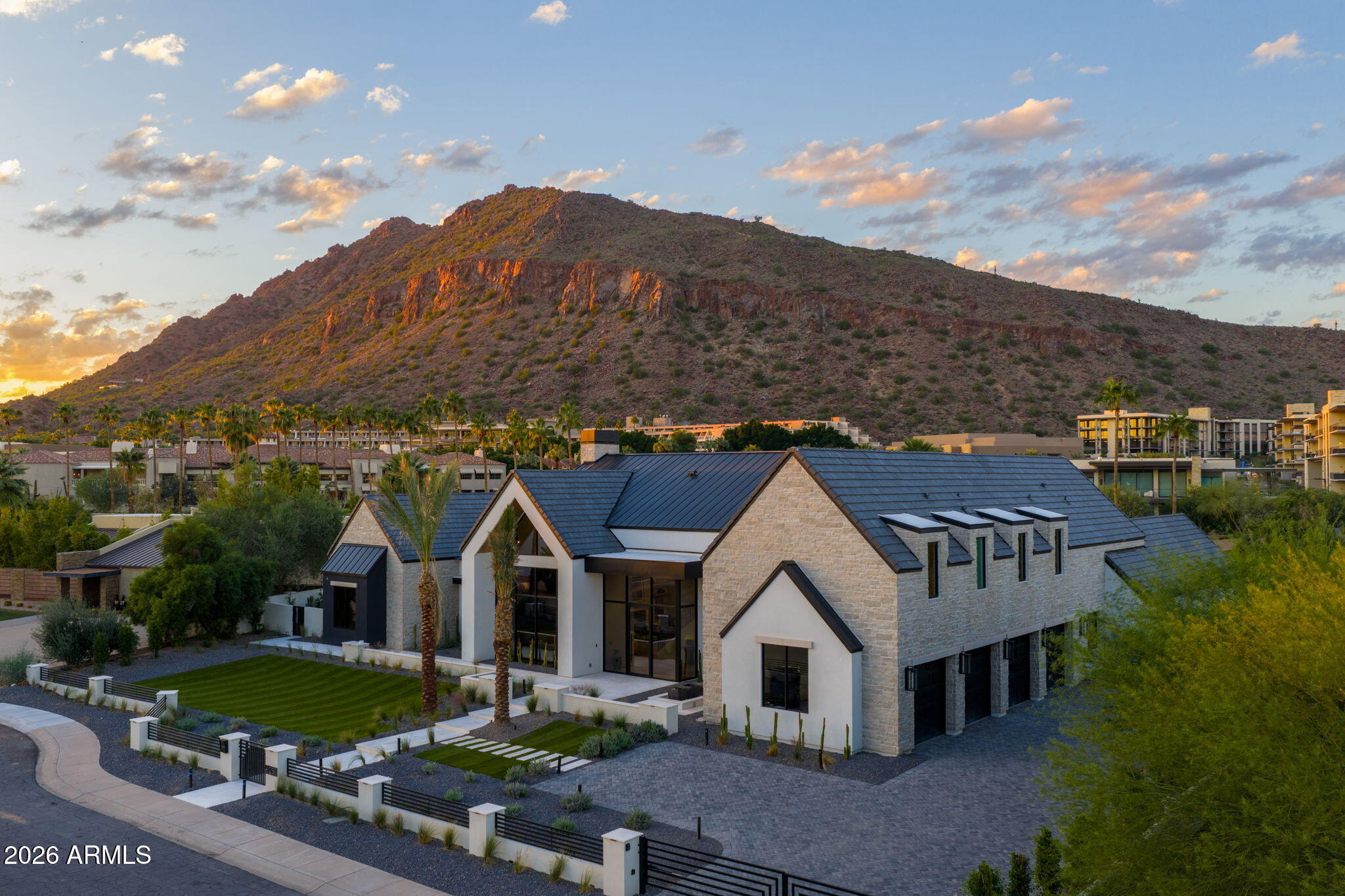 This privately gated custom estate, ideally located between Arcadia Proper and Paradise Valley in the prestigious Hopi School District, blends modern design with resort-style amenities. Inside, an impressive kitchen with a full back kitchen and pantry anchors the home, complemented by five en-suite bedrooms, a guest suite, office, fitness room, and pool house—balancing elegance with function. Outdoors, a sparkling oversized pool and spa, covered cabana, sunken firepit, and full sand volleyball court create a true resort retreat. Mature palms frame the property, while unobstructed Camelback Mountain views provide a striking backdrop. A spacious four-car garage and private motor court complete this rare Scottsdale offering.