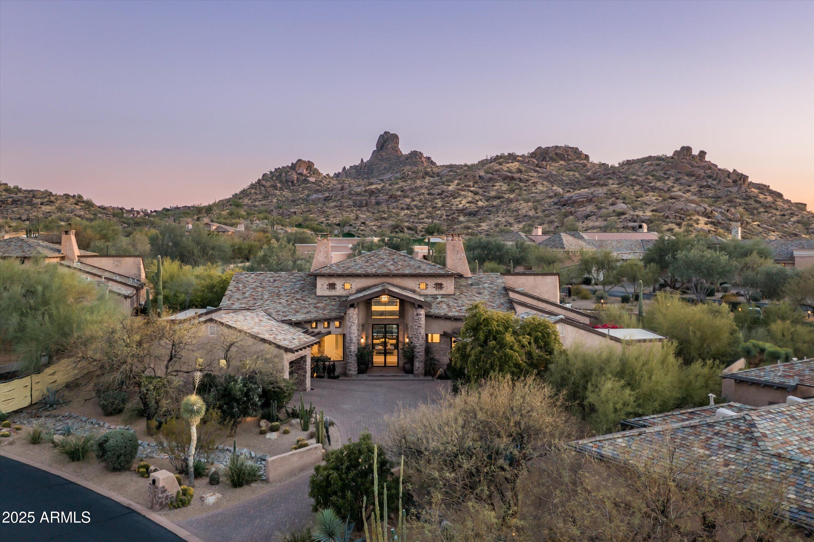 Completely remodeled and customized home in Estancia sited on a south-facing lot with Pinnacle Peak views | Reimagined in a chic expression of French Country-style by award-winning Ownby Design | The single-level floor plan includes an open kitchen with a living and family room, large primary suite, office/flex room and guest suite in the main house with 2 guest suites in the separate entrance guest house | Interior details include European white oak flooring, reclaimed ceiling beams, mortar-washed fireplace surrounds, custom plumbing and lighting fixtures and limestone tile accents | The outdoor living area includes a heated pool and spa, ramada sitting area with fireplace and built-in heaters, BBQ station and multiple dining areas | Conveniently located a short walk to The Estancia Club