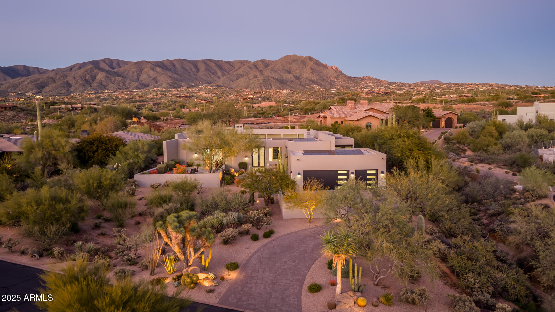 This modern luxury home showcases cutting-edge architectural design and sits on a premium north-facing golf course lot along the 5th tee of the prestigious Geronimo Golf Course and oriented perfectly to capture the surrounding mountain views. This home features an open-concept layout enhanced by expansive glass walls,  floor-to-ceiling sliding doors that frame breathtaking views from nearly every room, and multiple patios. Plus, owned solar panels for energy efficiency.  The formal living room centers around a sleek three-sided gas fireplace and surround sound.  Nearby, the dining room makes a striking statement with its illuminated floor-to-ceiling wine gallery. The modern kitchen is both stylish and functional, offering built-in stainless-steel appliances, a waterfall-edge island, and a breakfast bar perfectly positioned to enjoy mountain views through the corner window. The spacious primary suite includes custom built-ins and a luxurious ensuite featuring a soaking tub, dual-head tiled shower, direct access to the spa, and a custom closet with modern cabinetry. Each of the additional three bedrooms offers its own private ensuite. Outside, the property transforms into a Sonoran Desert oasis with a sparkling pool and spa, built-in BBQ, and a gas fire pit for relaxing evenings under the stars. Thoughtfully designed landscape lighting creates a stunning nightscape. Come experience this exceptional home in person!