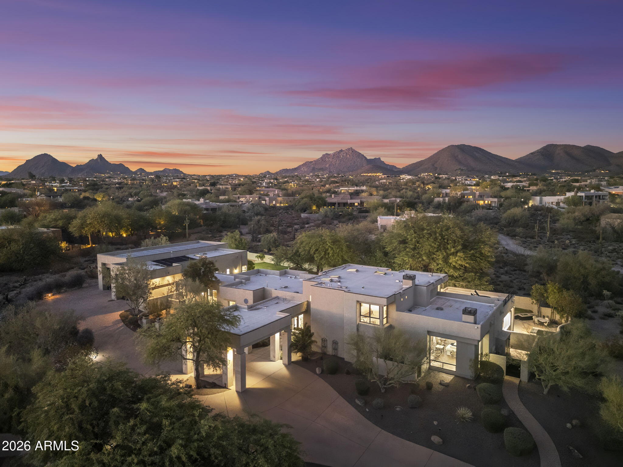 Tucked behind a private drive at the end of a quiet North Scottsdale cul-de-sac, this custom estate offers the kind of setting that feels private, elevated, and removed from it all, yet remains minutes from the best of 85255. Set on 1.56 acres with dramatic mountain, sunset, and city-light views, the property pairs impressive scale with a relaxed desert lifestyle. Spanning more than 7,800 square feet, the residence features 5 bedrooms, 5 bathrooms, and a floor plan designed for privacy, entertaining, and comfortable everyday living. Soaring ceilings, oversized windows, and generous living spaces create an open, light-filled atmosphere, while warm architectural details bring character and depth throughout the home. At the center of the home, the kitchen makes a strong impression with rich cabinetry, expansive counters, designer lighting, and excellent flow into the surrounding dining and living areas. Multiple gathering spaces give the home flexibility for hosting, relaxing, working from home, or creating separate areas for guests and family. The scale and layout also lend themselves beautifully to multigenerational living, with ensuite guest accommodations, multiple living areas, and private spaces that allow everyone to feel connected while still having room of their own. For car enthusiasts, the impressive garage space and collector-style setup offer a rare opportunity to showcase, store, and enjoy a prized collection at home. The primary suite is privately positioned and opens to its own balcony, capturing elevated city light views across the surrounding desert landscape. Guest bedrooms include ensuite accommodations, while additional spaces such as the wine room, game room, and entertainment areas add to the home's versatility. Outdoors, the property is designed to take full advantage of the Arizona setting. A sparkling pool, covered patios, view terraces, mature landscaping, grassy areas, and desert surroundings create a private resort-style environment with plenty of room to lounge, entertain, and enjoy the sunsets. With a porte-cochere arrival, expansive motor court, exceptional garage space, and a location close to North Scottsdale's top golf, dining, shopping, and trail systems, this estate delivers space, privacy, views, and presence in one of the area's most sought-after pockets.