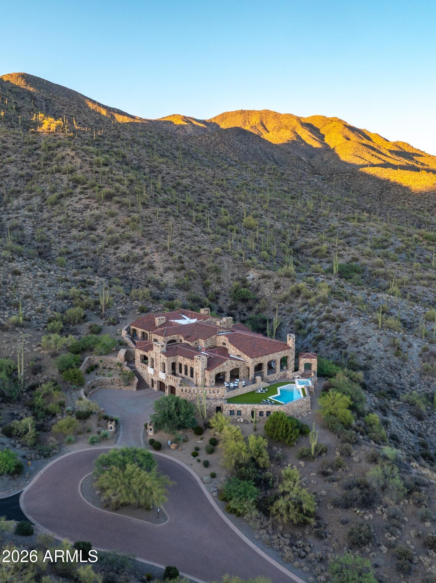 Perched high on a pristine, south-facing hillside spanning over 10 private acres, this architectural masterpiece offers an unparalleled living experience within the prestigious Desert Mountain Private Golf community. Designed by the renowned Lee Hutchison and flawlessly executed by Manship Builders, this 12,680-square-foot estate seamlessly blends commanding, panoramic valley views with the romantic allure of Old World elegance.
Every inch of this three-level estate speaks to uncompromising quality and meticulous curation. From the exterior's robust, low-maintenance full fieldstone facade to the custom ironwork and bespoke doors found throughout, the home is a testament to timeless artisan craftsmanship. Inside, the warmth of reclaimed wood floors pairs beautifully with rich natural stone setting a dramatic yet inviting tone. Navigating the homes expansive layout is effortless, thanks to a discreet private elevator servicing all three levels.

The gourmet chefs kitchen is a visual and functional triumph, anchored by a magnificent brick barrel ceiling and massive wood-topped center island that evokes European sophistication. Designed for both high-end entertaining and daily living, the culinary wing features top-tier appliances, premium finishes, and an incredibly spacious back pantry to keep preparation seamlessly out of sight.
The primary suite is a sanctuary of self-care. The ultra-luxurious bath functions as a private day spa, boasting dual dressing rooms, a deep lounge tub, and a restorative infrared sauna.

Your guests will enjoy the ultimate in privacy and comfort, with four generously sized ensuite bedrooms - each featuring its own private balcony overlooking the dramatic desert landscape.


Entertainment & Lifestyle Amenities: The lower level of the estate is dedicated to leisure, wellness, and socializing: The Cinema Experience: A state-of-the-art, 18-seat tiered theater brings the commercial cinema experience directly to your home. The Social Hub: A massive game room features a full-service bar, perfect for hosting cocktail hours or game nights. Golf & Fitness: Perfect your swing in the unfinished golf simulator room (ready for your custom specifications), and maintain your wellness regime in the dedicated fitness room. 

Additional amenities include a stately executive workspace designed for absolute privacy and productivity. A substantial 6-car garage to shelter your prized collection.

This estate is more than a home; it is a legacy property offering a rare combination of absolute privacy, architectural pedigree, and the resort lifestyle of Desert Mountain.