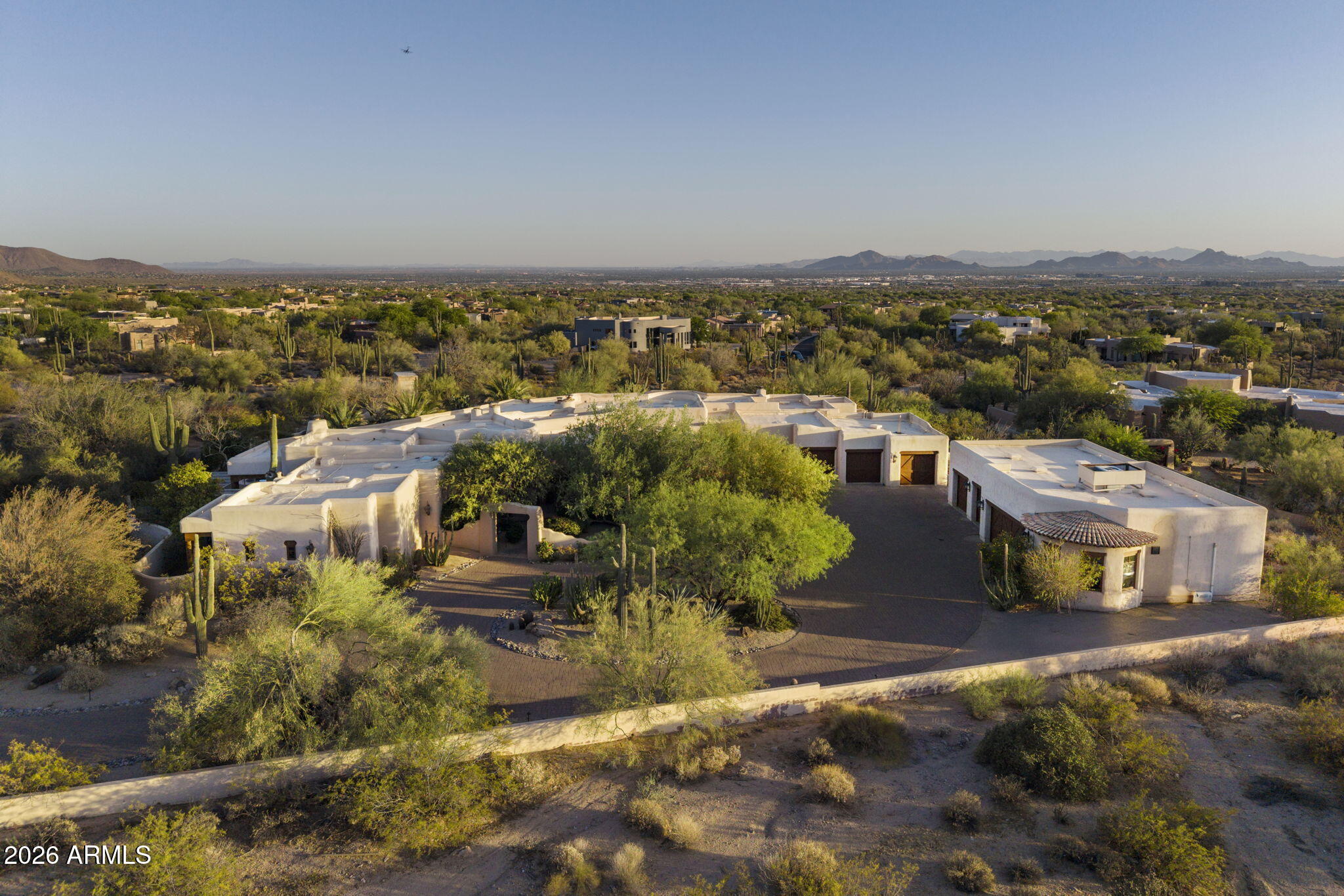 Perched atop more than 3 pristine acres in the exclusive Pinnacle Vista III community, this gated Santa Fe-inspired estate delivers breathtaking 360-degree mountain and city light views, exceptional privacy, and world class luxury living. A dramatic 1/8 mile winding paver driveway leads to an extraordinary resort-style compound designed for both grand scale entertaining and the ultimate vehicle collector lifestyle.

Encompassing almost 13,000 square feet under roof, the estate includes a 5,493-square-foot main residence, detached guest house, expansive covered outdoor living spaces, and garage capacity for up to 14 vehicles. The main residence showcases artisan Venetian plaster walls, hand-carved wood beams, soaring curved architecture, and seamless indoor-outdoor living. Designed with uncompromising craftsmanship, the home features 3 en suite bedrooms including a spectacular primary retreat with boutique-style dressing room and fitness space, a chef's kitchen with Viking and Sub-Zero appliances, refrigerated wine room, multiple fireplaces, and fully integrated smart-home automation.

A true centerpiece of the estate is the climate-controlled 10 car show garage, curated for the serious automotive enthusiast with custom color-changing LED lighting, travertine floors, cigar lounge with ventilation system, office, surround sound entertainment area, and showroom quality presentation throughout. An additional oversized air-conditioned 4-car garage, totaling 14 cars on property includes a dedicated detailing bay and private bath.

The detached guest house offers luxurious accommodations with full kitchen, high end appliances, fireplace, private patios, and refined custom finishes throughout.

The newly reimagined backyard acts as your own private resort with 3,500 square feet of covered patios, an oversized pool and spa, rock waterfall, Viking outdoor kitchen, outdoor media and sound systems, misting features, lush landscaping, and iconic saguaro cacti framing the spectacular desert views.

Complete with grandfathered horse privileges this is truly an extraordinary opportunity to own one of North Scottsdale's most unique and unforgettable luxury compounds.