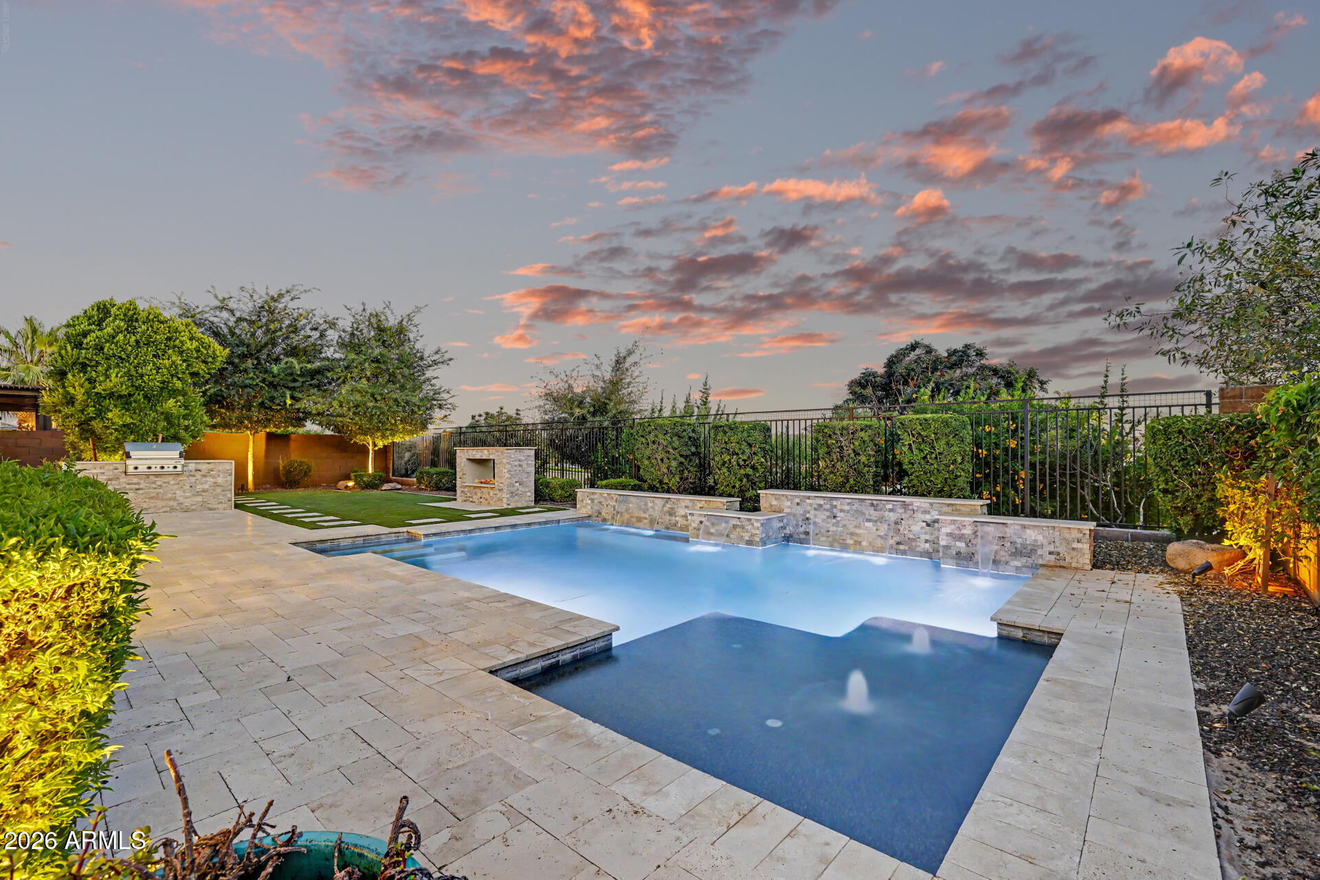 Situated on an interior north/south lot backing to a greenbelt in the gated Estates community within the award-winning Eastmark master-planned community, this luxury East Mesa home offers privacy, upgraded finishes, and resort-style outdoor living. The split floor plan features 3 bedrooms plus a dedicated den, making it ideal for a home office, flex space, or guest needs. Interior upgrades include 10-foot ceilings, plantation shutters throughout, surround sound with in-ceiling speakers, upgraded luxury vinyl plank flooring, and upgraded 5-inch baseboards. Designed for indoor-outdoor living, the spacious family room features a 3-panel sliding glass door opening to the backyard retreat. The gourmet kitchen includes a large island with breakfast bar, quartz countertops, subway tile backsplash butler's pantry, extensive 42-inch cabinetry with hardware and crown molding, and stainless-steel appliances including a gas cooktop, wall oven, and built-in microwave. A private side courtyard off the kitchen creates an additional entertaining space, while the laundry room includes a gas dryer hookup for added convenience. The spacious owner's suite features 10-foot ceilings and a spa-inspired bathroom with a large walk-in shower and oversized walk-in closet. Both secondary bedrooms are generously sized and include walk-in closets. Step outside to a true resort-style backyard with no neighbor behind and open greenbelt views. The large, covered patio with travertine decking and ceiling fan overlooks a heated Pebble Tec pool with baja step, water feature, and in-ground cleaning system. Additional outdoor features include synthetic grass, a built-in fireplace with stone surround, and a view fence that enhances the open feel and privacy. The gated Estates at Eastmark offers exclusive community amenities, including a resort-style pool with lap lanes, clubhouse with fitness studio, event lawn, outdoor fire pits, shaded playgrounds, and walking trails connecting throughout the community and to Eastmark Great Park. If you're searching for a luxury home in East Mesa, gated community living in Eastmark, or a home with a resort backyard and greenbelt lot, this property delivers location, lifestyle, and upgraded living in one of the area's most sought-after master-planned communities.