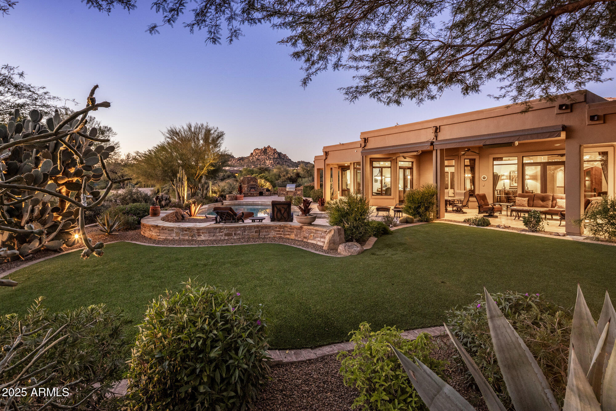 Welcome to a custom-built residence that epitomizes classic Arizona living in exclusive Windy Walk Estates of Troon. Perfectly positioned along the third green of the prestigious Troon Country Club golf course, this single-level home captures breathtaking views of North Scottsdale's iconic Pinnacle Peak, city lights & the lush golf course.  A private desert landscape & elegant circular drive leads to a residence where craftsmanship & comfort unite. Inside, timeless design unfolds through hand-finished walls, rich alder cabinetry, custom built-ins & natural stone finishes that exude warmth & elegance. The chef's kitchen impresses with a generous granite island, double ovens & custom cabinetry including built-in desk - seamlessly opening to the inviting great room & formal living areas, all perfectly oriented to frame the stunning views beyond.  Walls of glass & French doors invite natural light & effortless indoor/outdoor living, opening to the backyard.  A true oasis, complete with expansive lounging areas, pool & spa surrounded by stone decking, fireplace & built-in barbeque, all overlooking the iconic desert scenery & green beyond that defines North Scottsdale living.  Designed for both quiet relaxation & grand entertaining, the outdoor spaces perfectly capture the essence of resort-style living.  Showcasing the ever-changing panoramas of fiery Arizona sunsets & glittering city lights, expansive patios with multiple seating & dining areas create year-round comfort & effortless opportunities for gatherings both large & small.  Inside, every bedroom is thoughtfully appointed as a private suite, including the rare luxury of 2 primary retreats, offering unparalleled comfort & privacy for family & guests alike.  Together, these refined interiors & resort-inspired exterior create a sanctuary of serenity, all within moments of North Scottsdale's finest dining, shopping & world-class golf.  Whether enjoying a quiet morning coffee as the sun rises over Pinnacle Peak or hosting an evening gathering under the desert stars, this home delivers an unmatched sense of serenity, beauty & connection to its surroundings.  Timeless architecture, stunning views & Troon's premier golf lifestyle come together in perfect harmony for those seeking an extraordinary experience of refined elegance, natural beauty & resort-inspired living in one of North Scottsdale's most coveted settings.