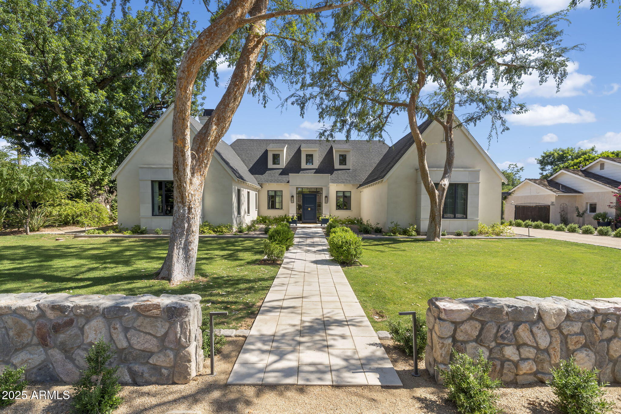 In the heart of North Central Phoenix's most coveted enclave, Rancho Solano, discover a residence where architectural pedigree, masterful craftsmanship, and elegant design converge. 325 W. Solano Drive is a one-of-a-kind home designed by award-winning architect Mike Higgins (PHG Master of the Southwest) and meticulously built by Tim Mann of TM Construction—two names known for shaping Arizona's finest homes.
Privately set behind artisan-crafted walls and glowing Bevolo gas lanterns, the 3,826 sq ft main house is complemented by 576 sq ft of detached quarters—ideal as a guest retreat, design studio, or private office. The custom front door opens into a foyer that immediately sets the tone: white rift and quarter-sawn oak floors with a hand-painted tile in-set by Tabarka Tile, millwork-clad walls, and warm Visual Comfort art lighting.

The great room impresses with a soaring cathedral ceiling, cross beams in rift-sawn white oak, and chevron-laid oak floors. The ambiance is effortlessly elegant, with handcrafted millwork and perfectly scaled chandeliers anchoring the space. The adjoining kitchen is a masterclass in understated luxury: custom inset cabinetry in a mix of rift oak and white dove, soapstone countertops, a fully integrated Sub-Zero refrigerator, Wolf appliances, and a retractable-door bar cabinet that elevates both function and form. Every detail from the Armac Martin hardware to the hand-painted Tabarka Tile backsplash has been thoughtfully chosen.

Each secondary bedroom is generously appointed with ensuite baths, built-ins, and custom window seats. The den, painted in Farrow & Ball Hague Blue, offers a dramatic retreat anchored by a Calacatta Setai marble fireplace, floor-to-ceiling millwork, and tailored bookcases. The primary suite is a serene retreat with vaulted ceilings and a fireplace with a Tabarka Tile surround and white oak mantle. The spa-like bath is finished in marble and Kallista fixtures, with a free-standing tub and reeded oak cabinetry. The walk-in closet by California Closets, includes a built-in vanity, Morris & Co. wallpaper, and boutique lighting.

The detached quarters reflect the same caliber of design, with vaulted ceilings, terrazzo tile, walnut and white dove cabinetry, and Herman Miller lighting. With a kitchenette and ¾ bath, it's as functional as it is beautiful.

Outdoors, a standing seam metal roof shelters the rear patios and detached quarters, while a sculptural painted brick fishpond, stacked brick chimney, and an exterior fireplace handcrafted in DC Cobble create rich visual focal points. Lush plantings and a garden courtyard lend a sense of softness and continuity, blurring the line between architecture and nature.

Additional features include a whole-house water filtration system, a stand-up attic with a lift, Emtek hardware, and custom designed doors by Doorworks throughout. From architectural detailing to material selection, every inch of 325 W. Solano Drive reflects restrained luxury and enduring design. An extraordinary offering in the heart of North Central Phoenix.