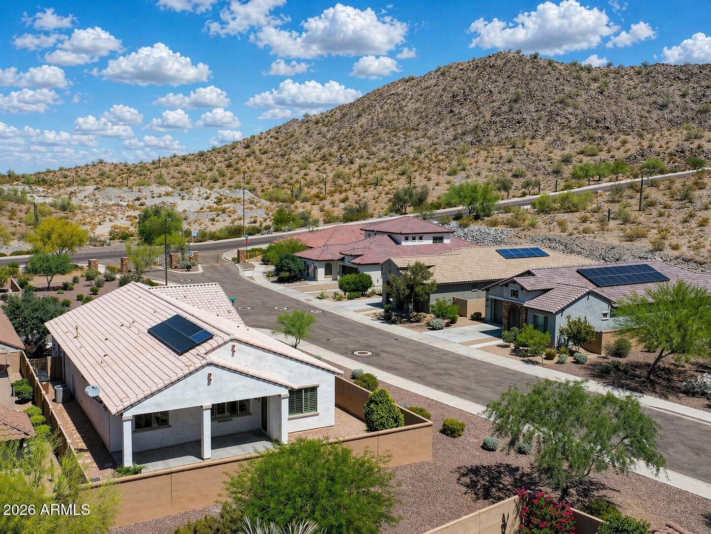 Tucked inside the gated Golf Ridge community of Estrella, this former model home blends thoughtful design with everyday comfort. Offering 3 bedrooms, 2.5 baths, and a versatile flex space ideal for a home office or den. The layout is both functional and refined. From the moment you step inside, soaring ceilings and a tray-detailed foyer create an inviting first impression. The heart of the home is a beautifully appointed kitchen featuring rich maple cabinetry, quartz countertops, a large island with breakfast bar, walk-in pantry, and S/S appliances including gas cooking. The open great room design makes it ideal for both entertaining and relaxed living. The primary suite offers a unique and convenient connection to the laundry room (washer & dryer included), while the secondary bedroom share a Jack-and-Jill bath, each with its own private vanity and spacious walk-in closet. Additional highlights include plantation shutters, surround sound, updated interior paint (2023), and a 2-car garage with extensive cabinetry. Energy efficiency is a bonus with a prepaid solar system helping keep utility costs down. Situated on a desirable corner lot with no direct rear neighbor just a peaceful common area behind the backyard offers an extended covered patio and low-maintenance landscaping, perfect for enjoying Arizona evenings. Out front, a paver driveway, mature landscaping, and a charming porch with mountain views create standout curb appeal. Life in Estrella means access to resort-style amenities including golf, lakes, pools, fitness centers, scenic parks, and miles of hiking trails all surrounded by stunning mountain views.